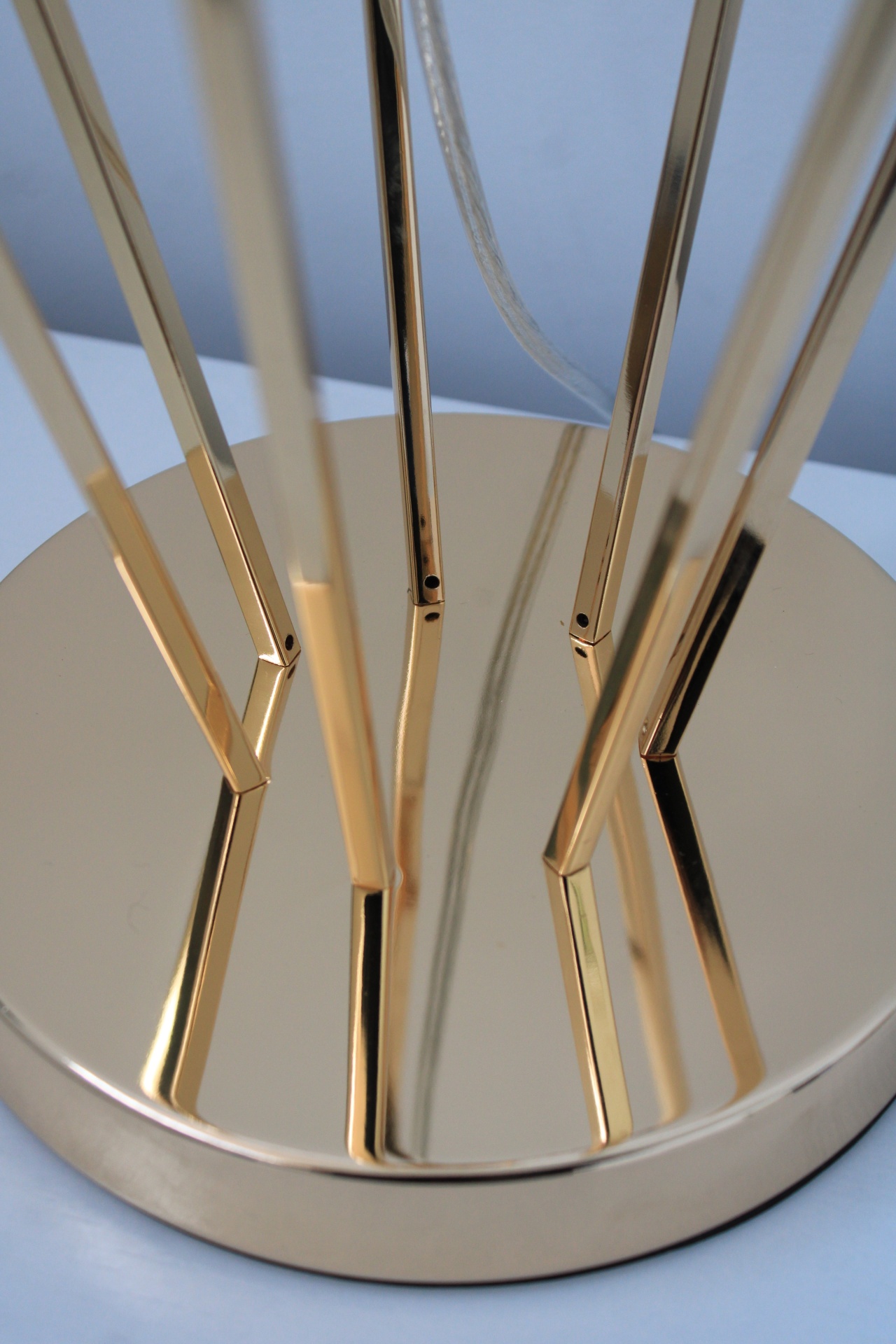 Base redonda metálica dourada com hastes angulares e cabo transparente