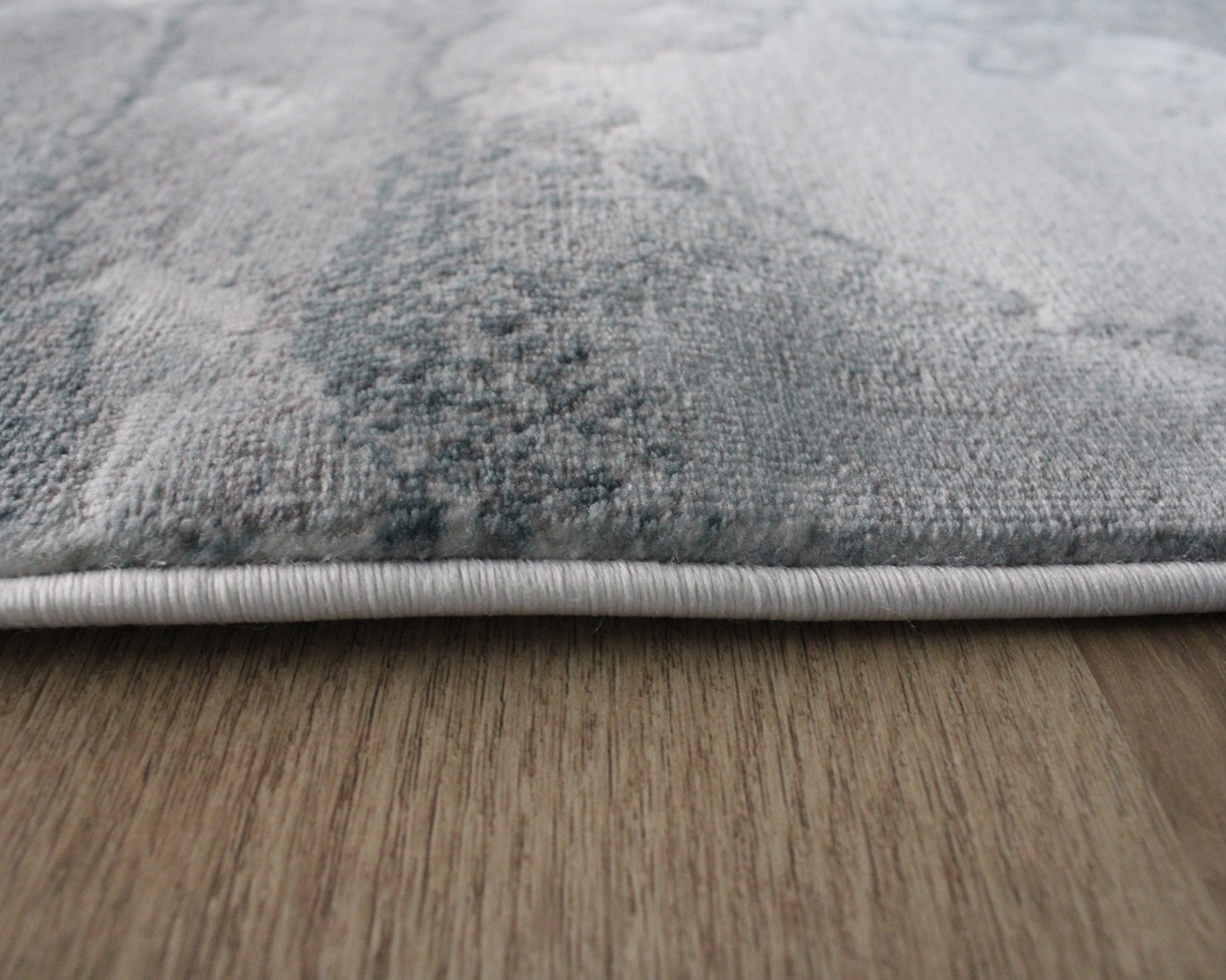 Tapete cinzento com padrão abstrato e borda costurada sobre piso de madeira