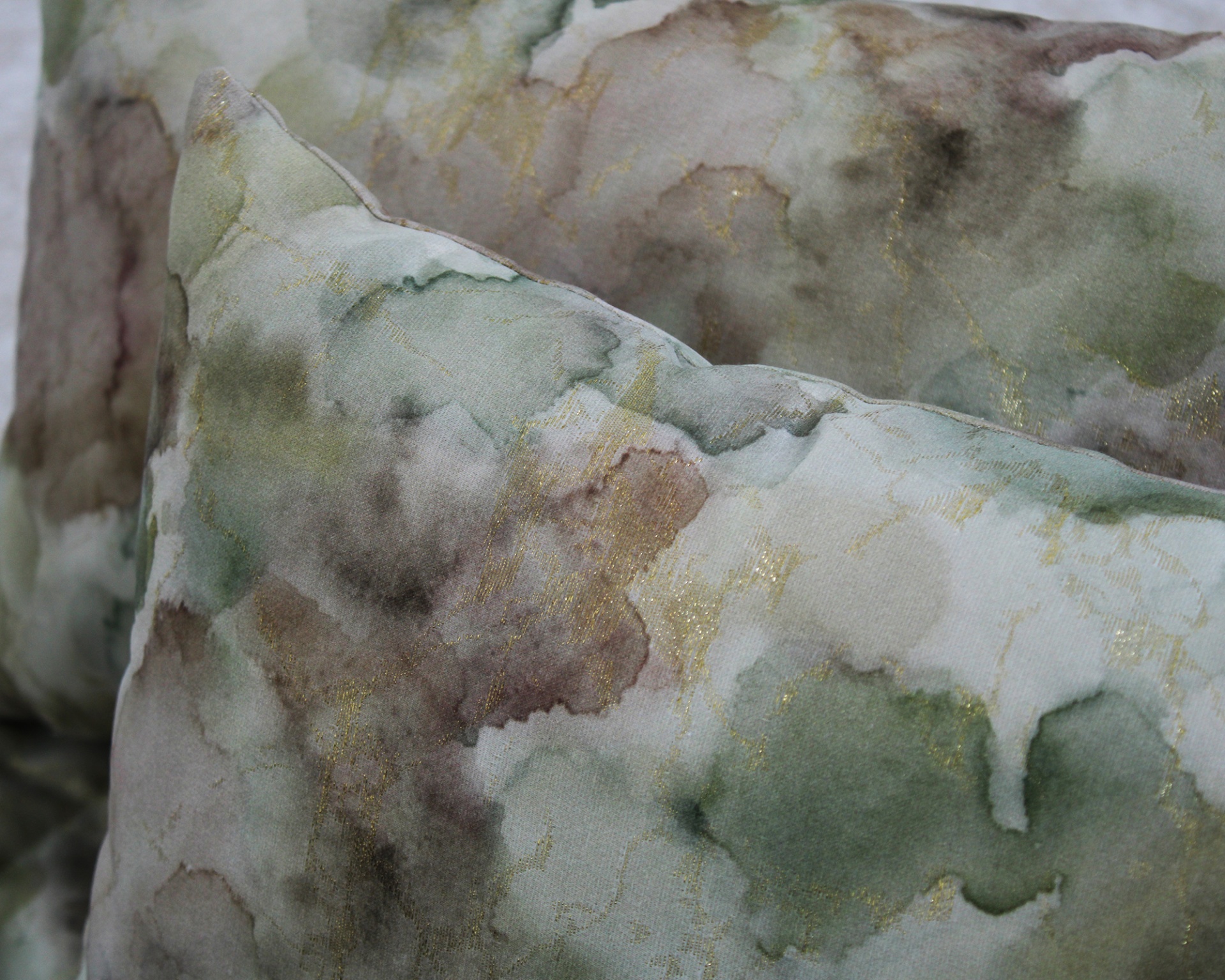 Almofadas decorativas com padrão em aguarela em tons verdes, castanhos e bege com detalhes dourados