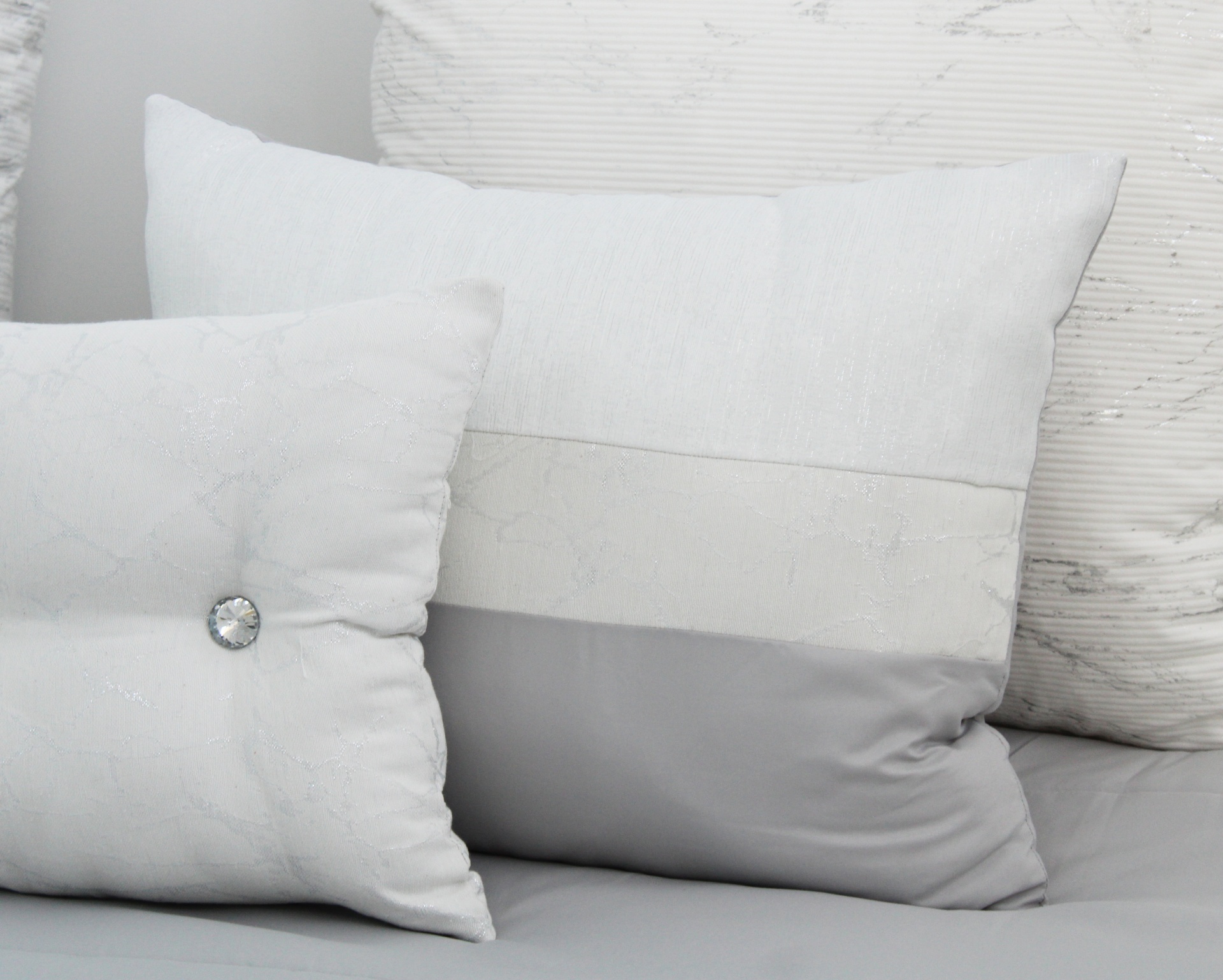 Três almofadas brancas e cinza com diferentes texturas e botão decorativo