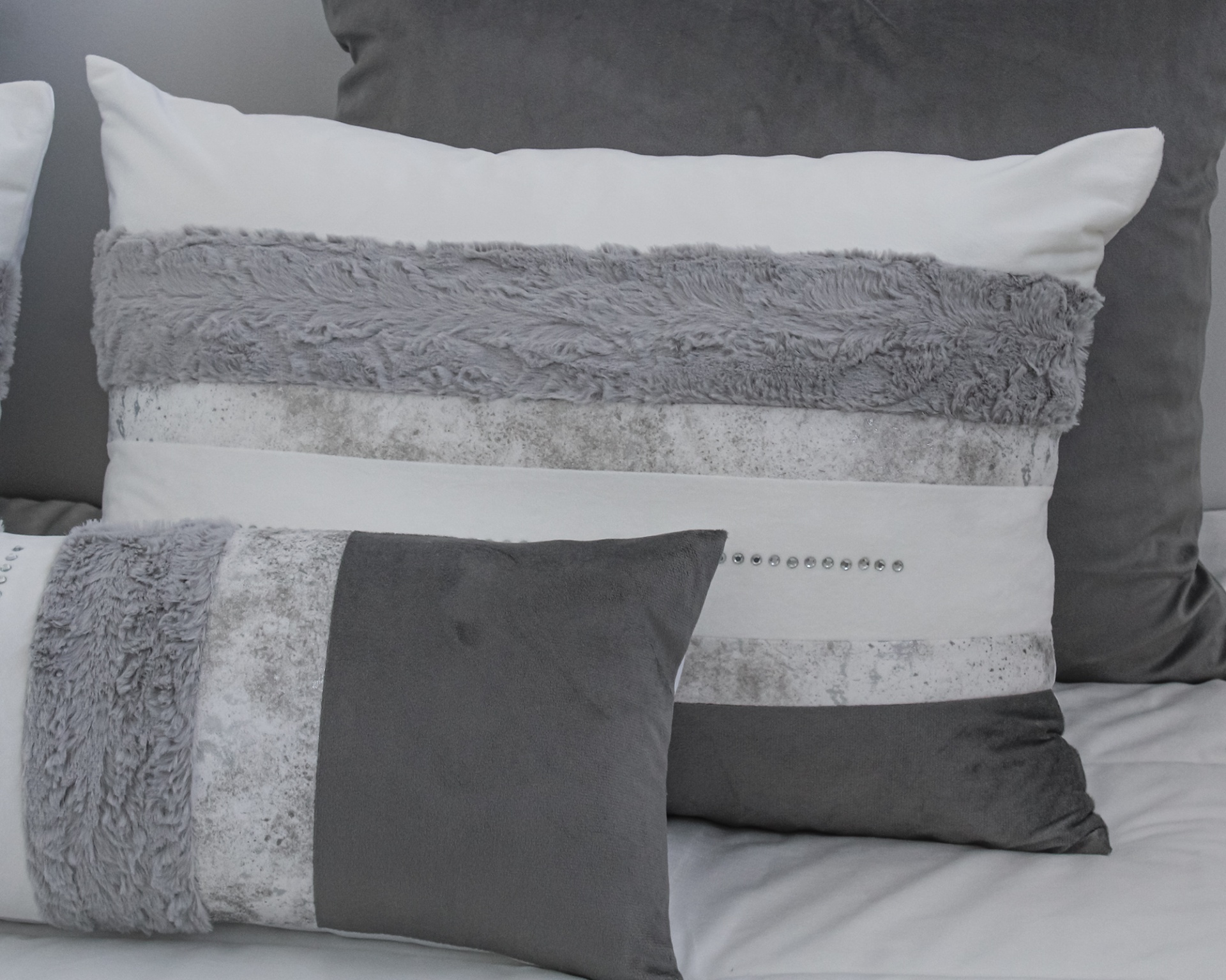 Duas almofadas decorativas cinza e branco com texturas variadas e detalhes brilhantes.