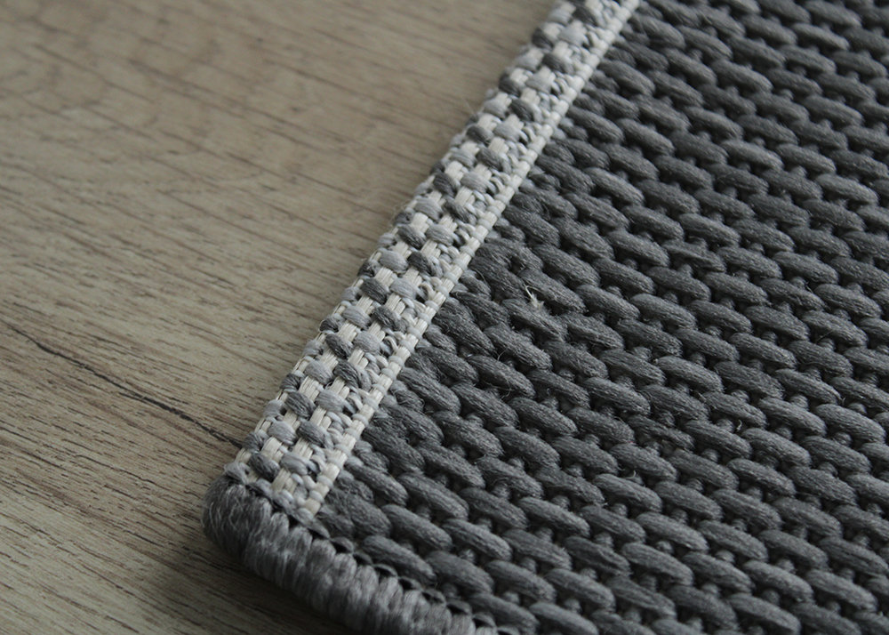 Tapete cinza tricotado com borda branca e cinza sobre piso de madeira clara