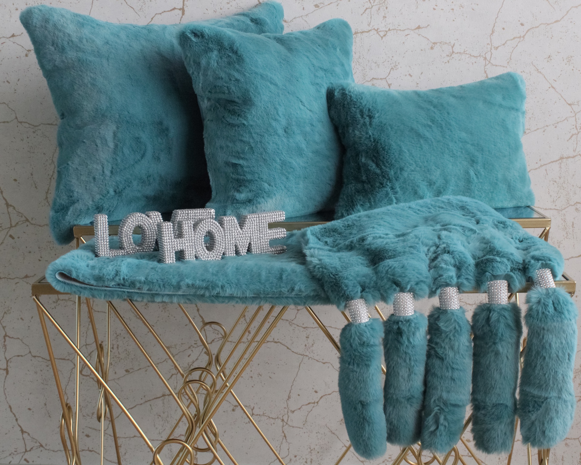Almofadas e manta peluda azul-turquesa com tasséis em mesa dourada moderna.