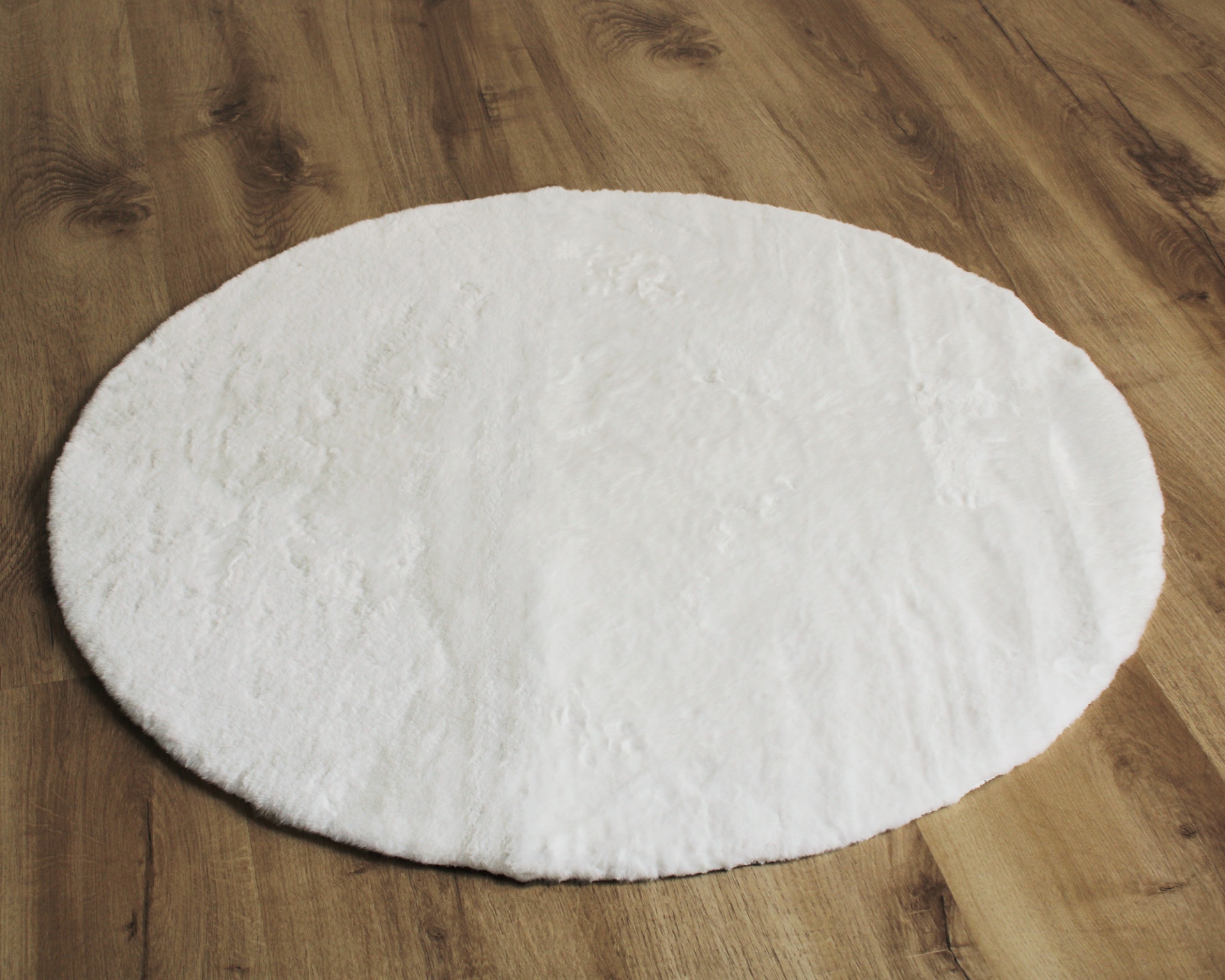 Tapete oval branco felpudo sobre chão de madeira clara