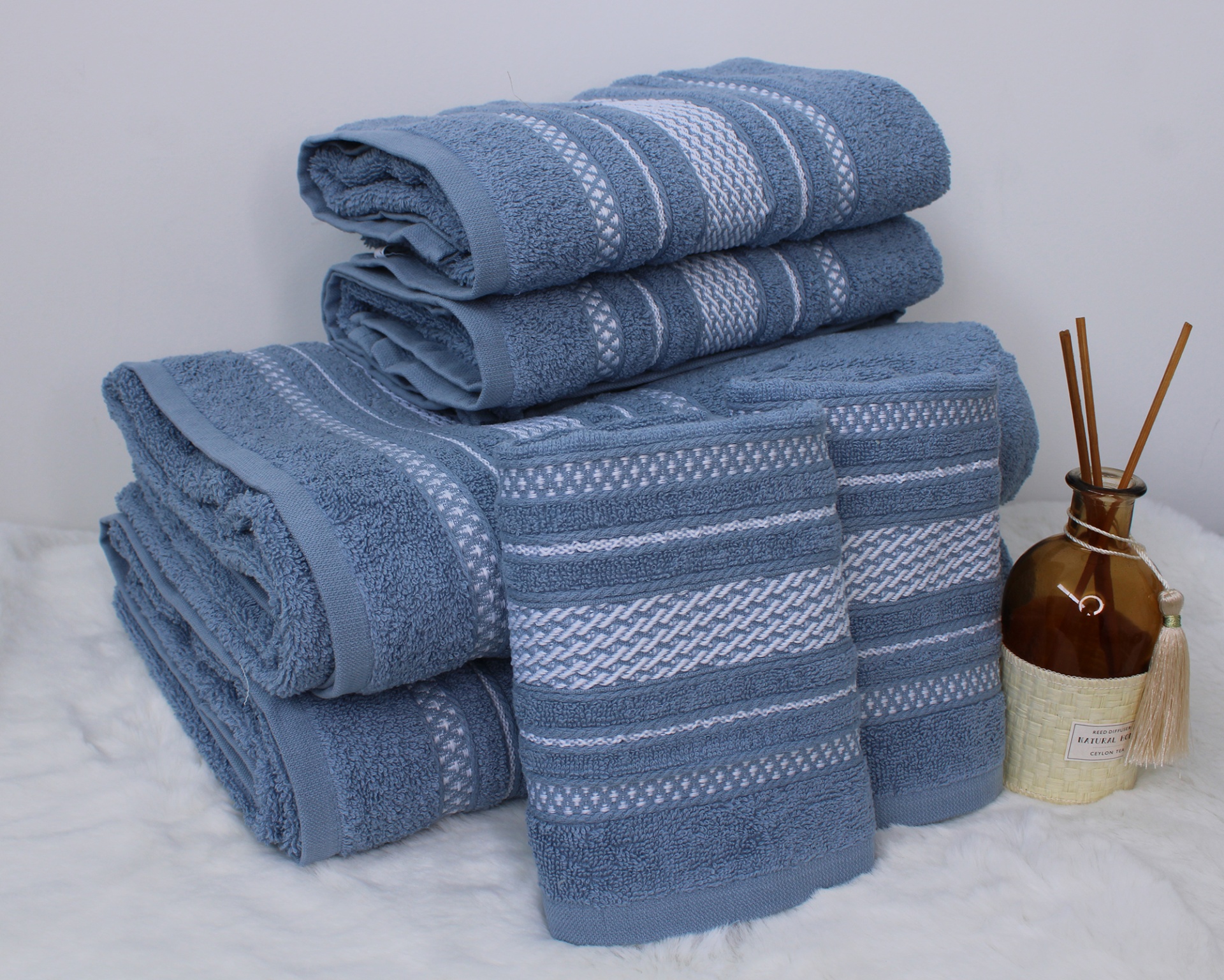 Conjunto de toalhas de banho azuis com padrões brancos e frasco decorativo castanho com palitos.