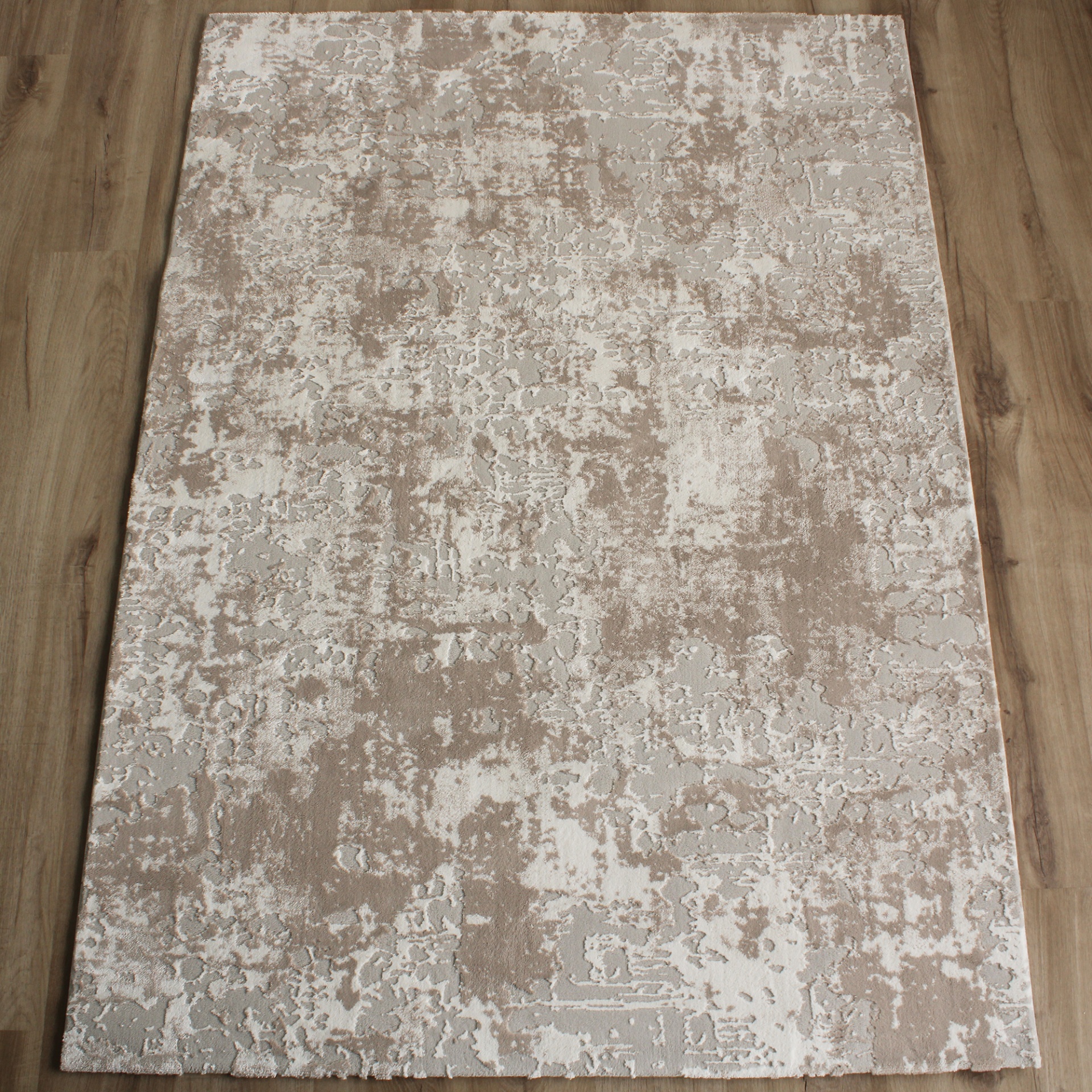 Tapete rectangular com padrão abstrato em bege, cinzento e branco sobre chão de madeira