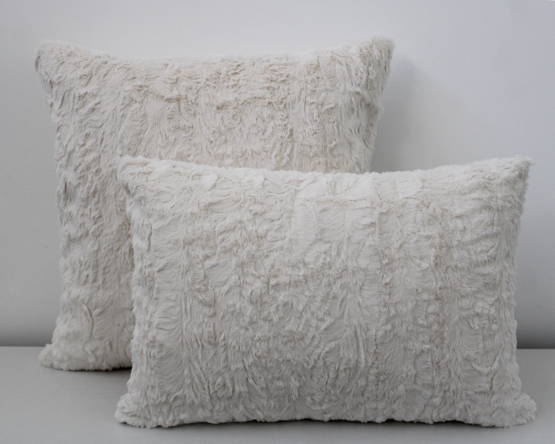Duas almofadas peludas brancas, uma retangular e outra quadrada, texturizadas, sobre superfície cinza