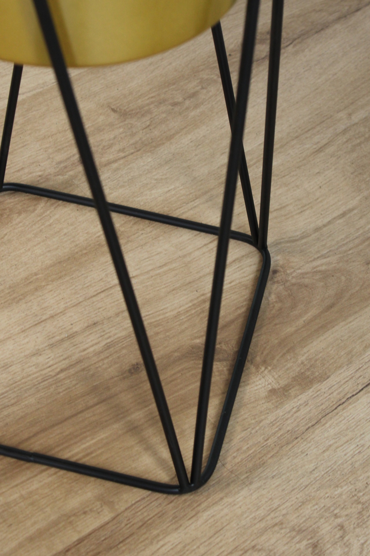 Base de suporte preta com objeto amarelo e chão de madeira