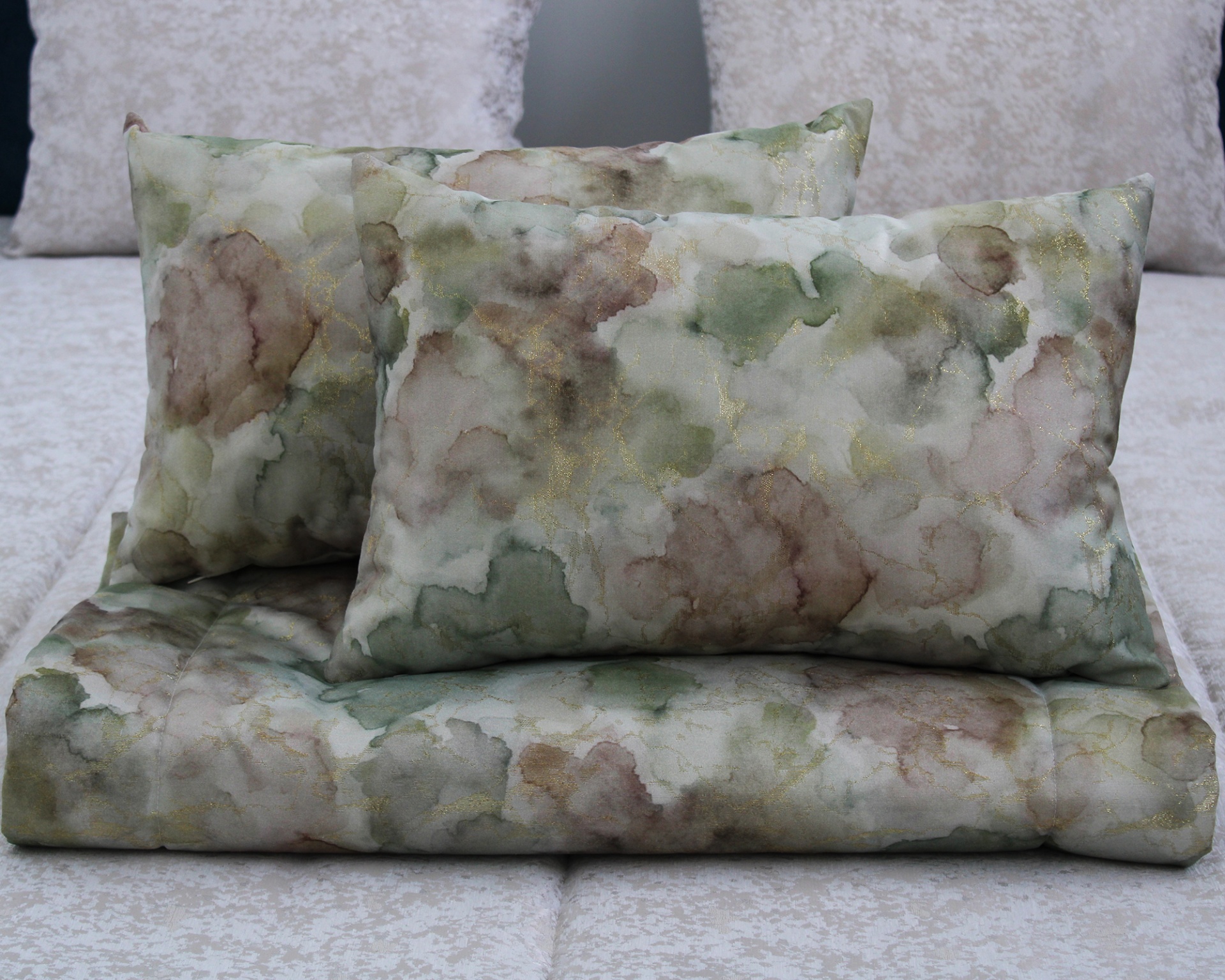 Almofadas e edredão padrão aquarela tons verde bege castanho detalhes dourados sobre cama beige