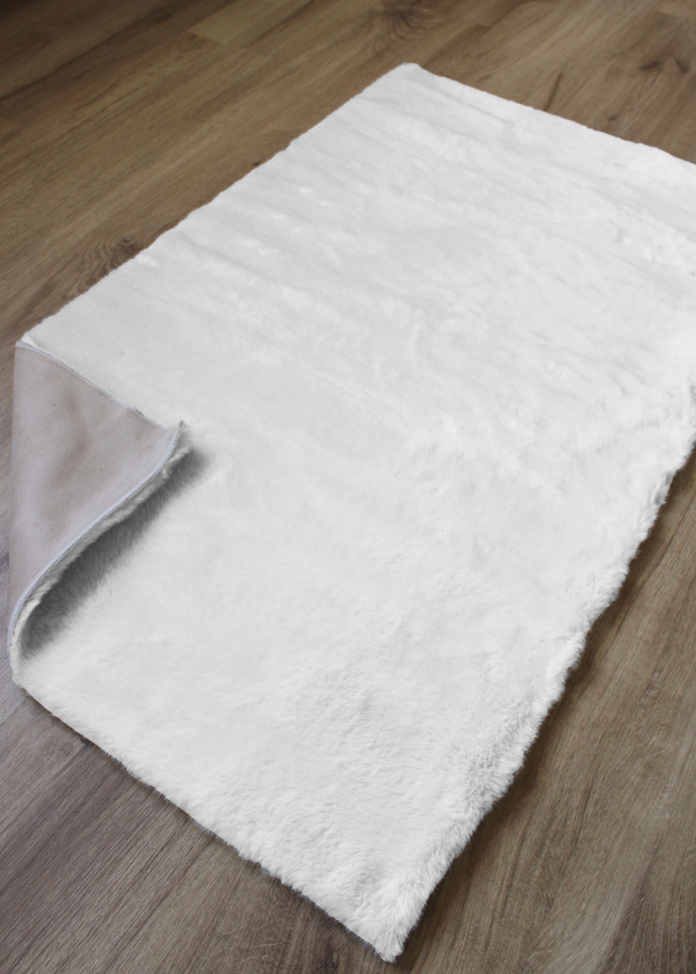 Tapete branco macio com verso cinzento em chão de madeira