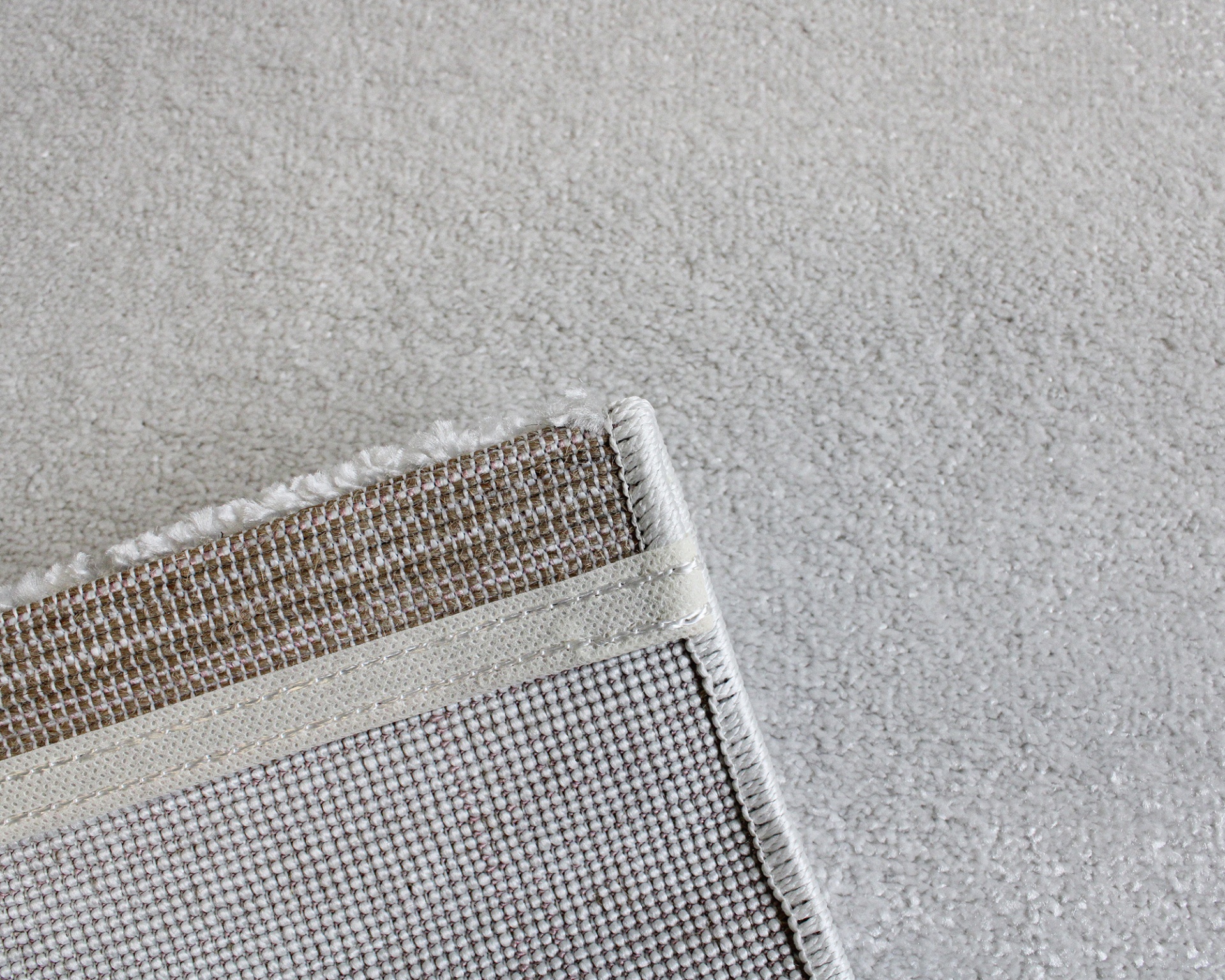 Canto de tapete bege claro com textura felpuda sobre chão cinza claro texturizado