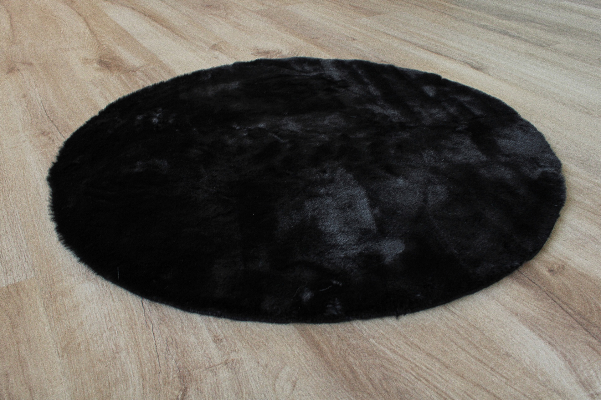 Tapete redondo preto felpudo em chão de madeira clara
