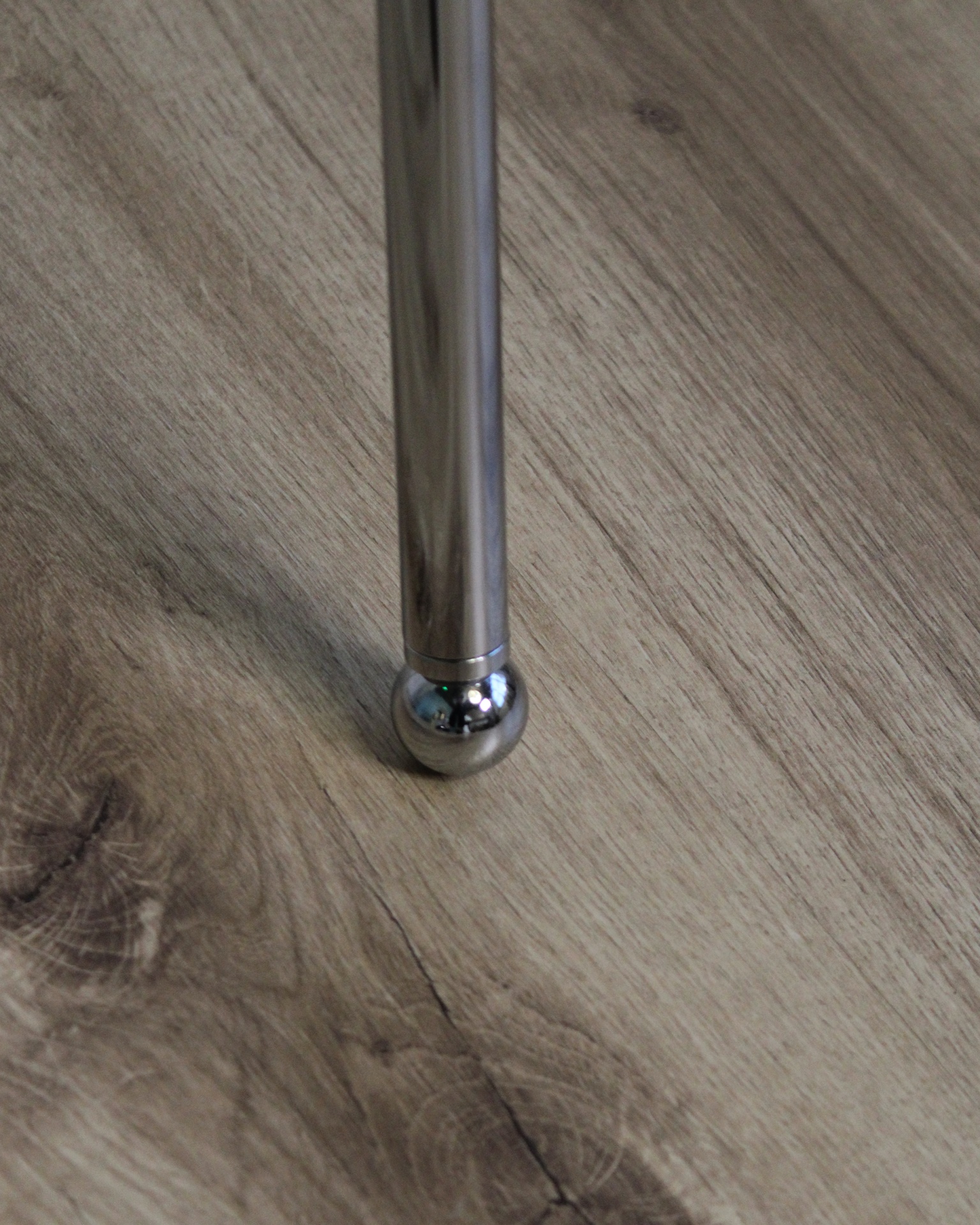 Pé de móvel cilíndrico em metal cromado sobre chão de madeira clara