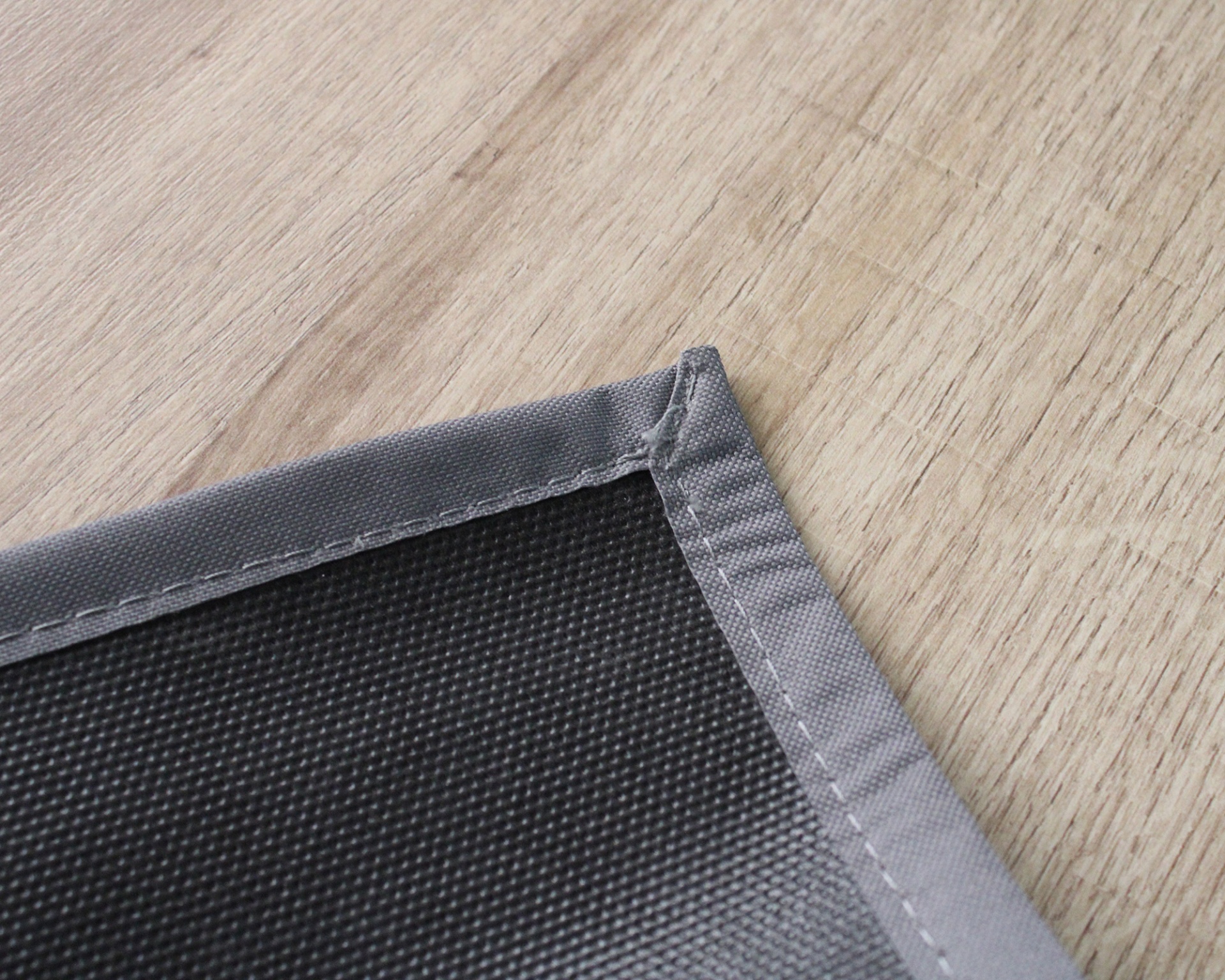 Ponta de tapete cinzento escuro com borda costurada em superfície de madeira clara
