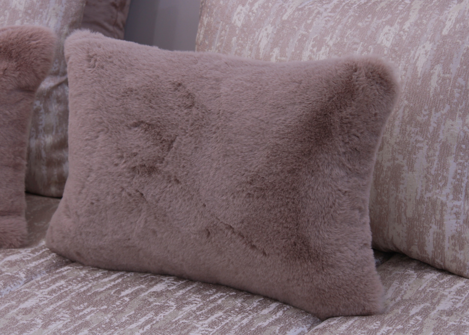 Almofada retangular rosa claro com textura felpuda num sofá rosa claro com padrão