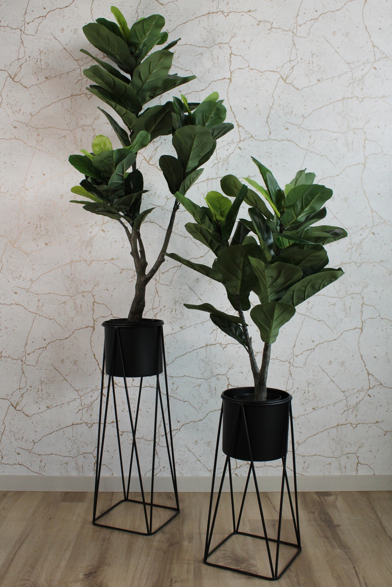 Dois vasos com plantas verdes em suportes metálicos pretos sobre chão de madeira clara