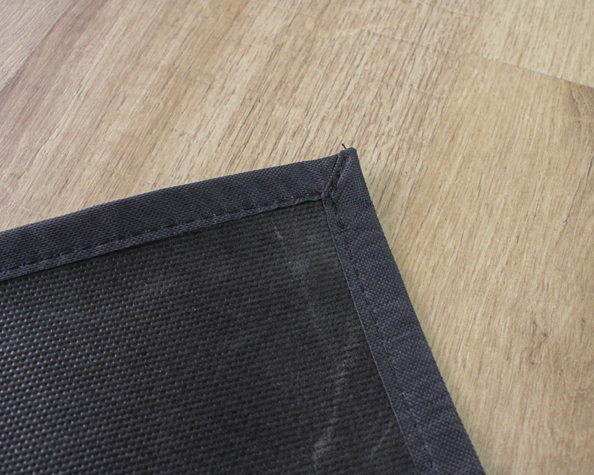 Tapete preto com bordas costuradas sobre chão de madeira clara