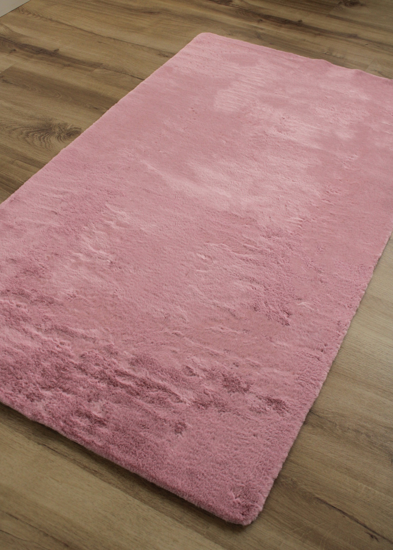 Tapete retangular cor-de-rosa com textura macia sobre chão de madeira claro