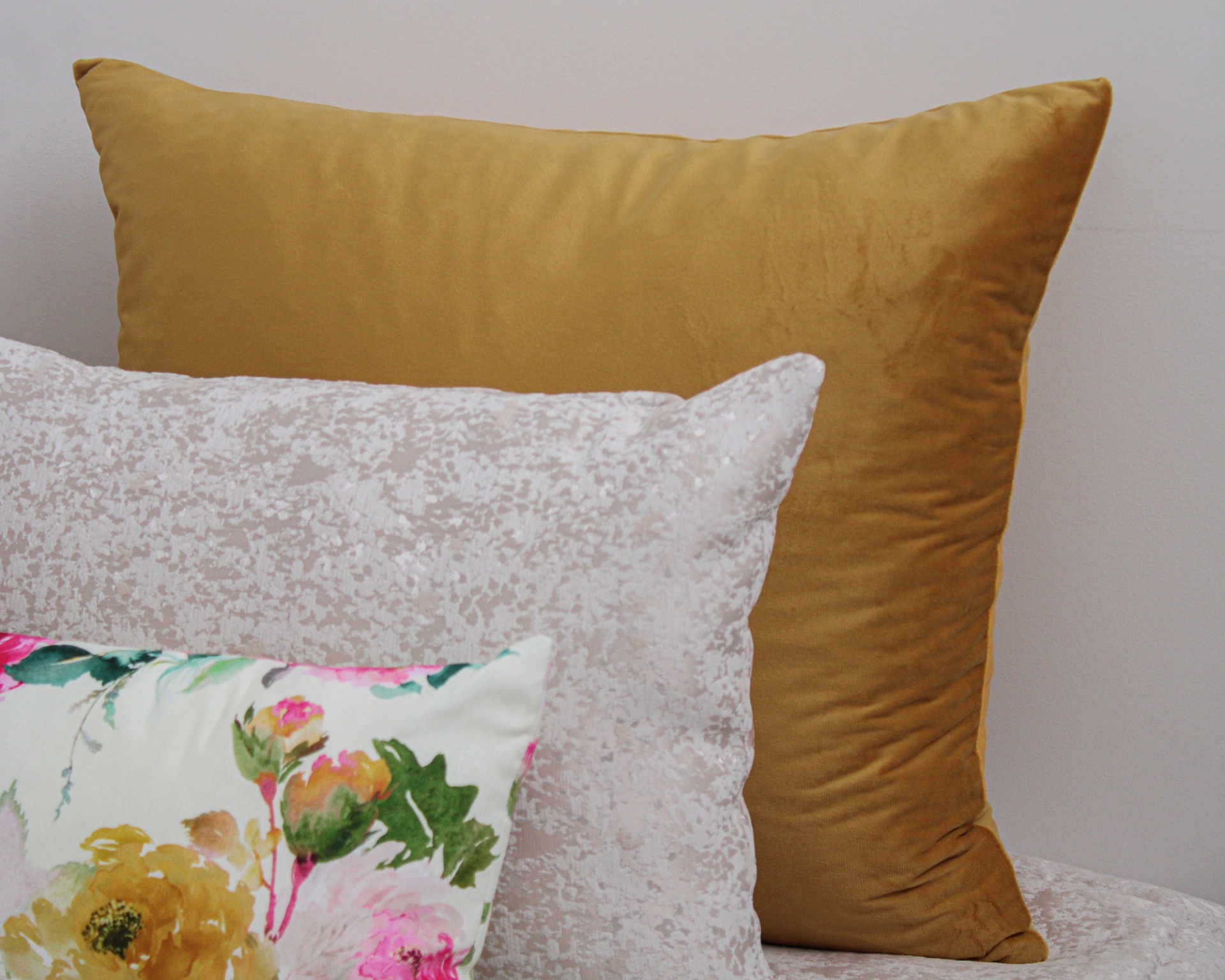 Três almofadas com veludo mostarda, padrão cinza e floral colorido
