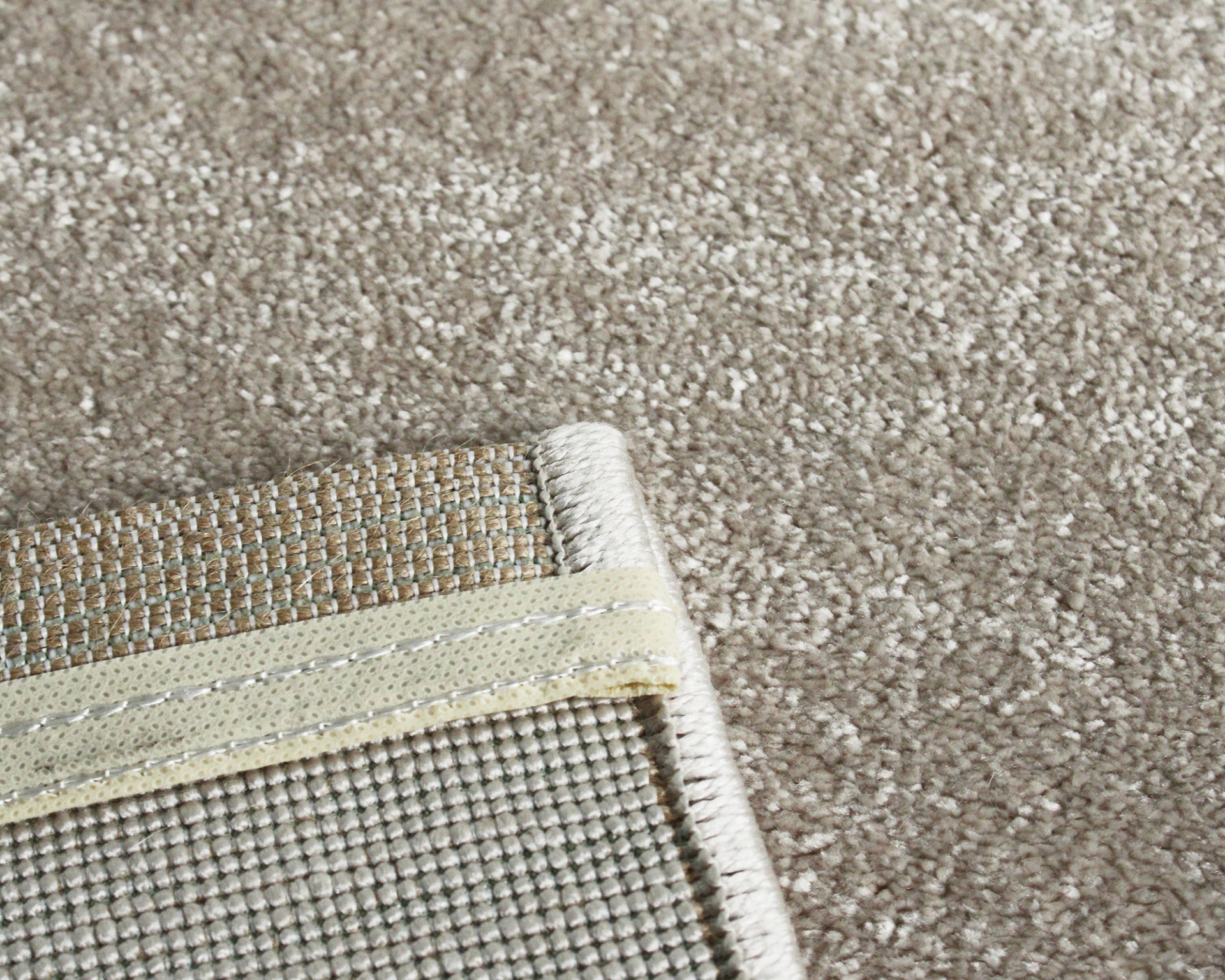 Tapete bege claro com canto dobrado mostrando verso e reforço