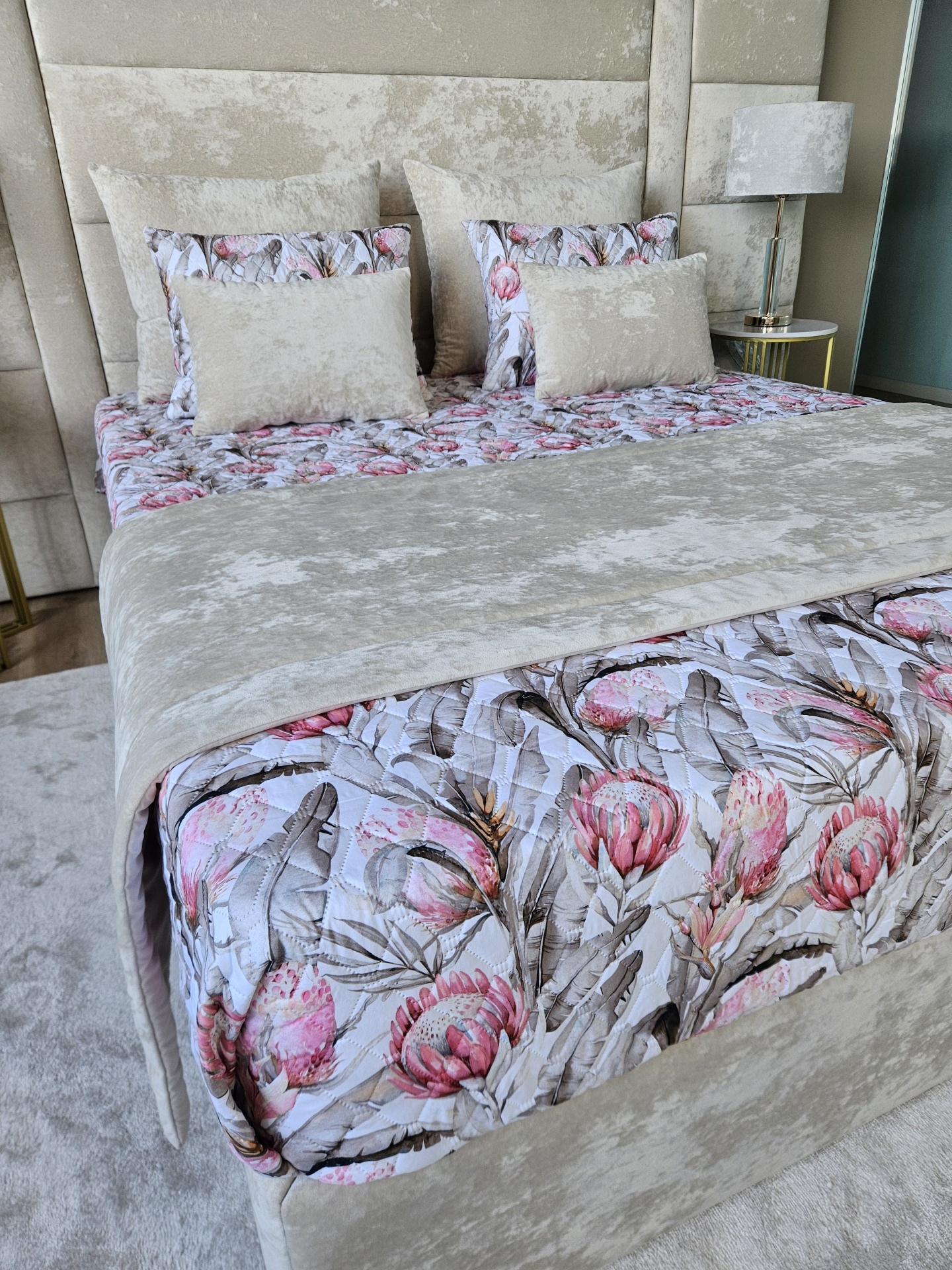 Cama com colcha floral e almofadas bege em quarto moderno com abajur cinza