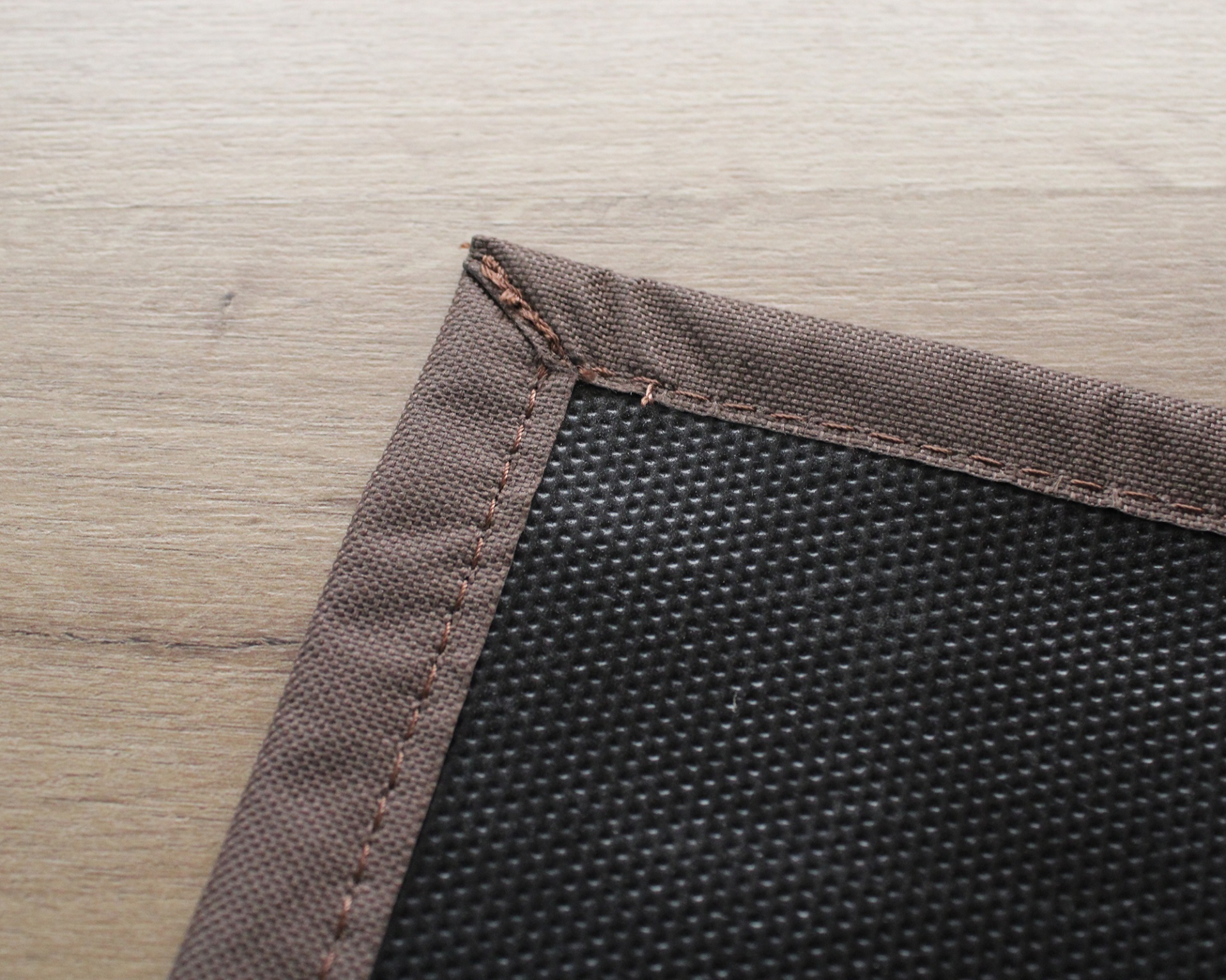Detalhe de tecido preto texturizado com borda castanha costurada