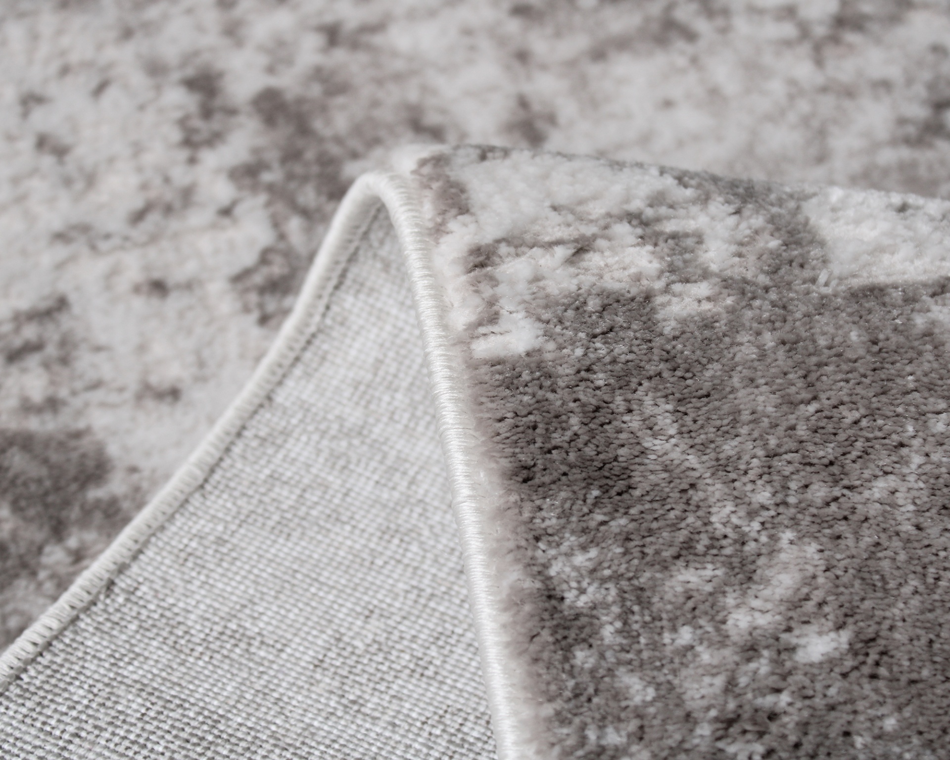 Tapete felpudo cinza e branco com padrão abstrato e bordas costuradas