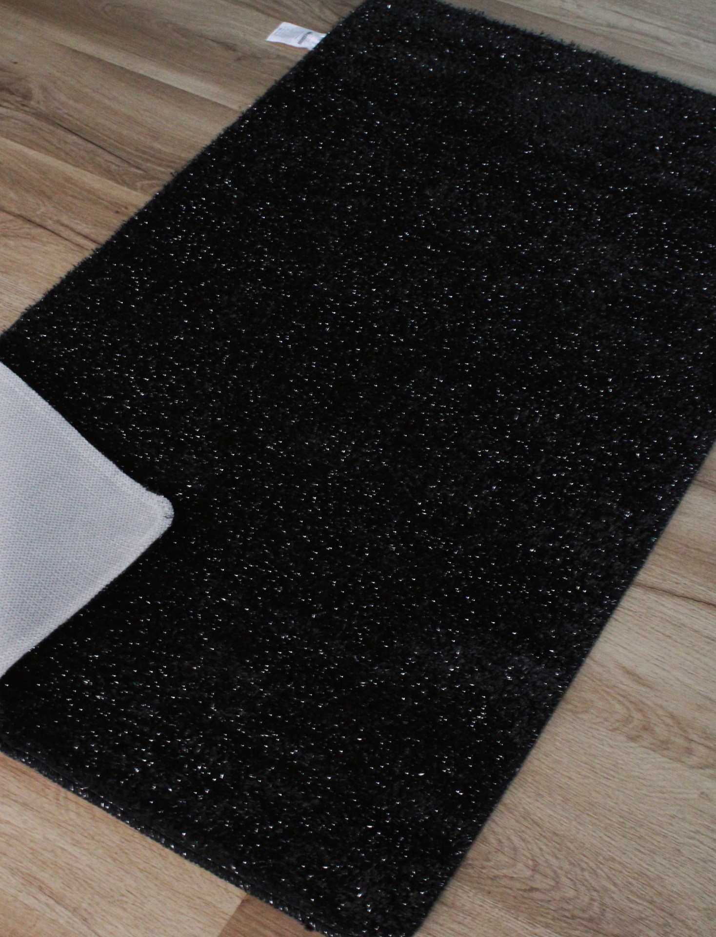 Tapete preto com textura brilhante e pormenores prateados sobre piso de madeira
