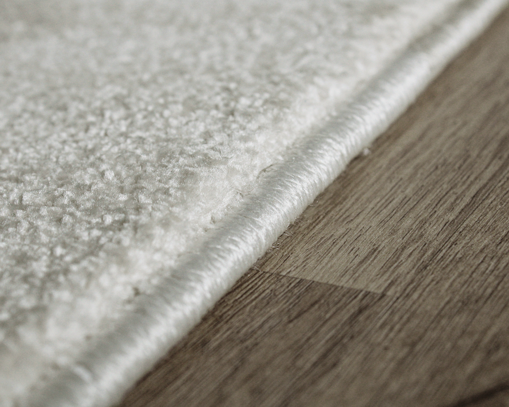 Detalhe de tapete branco felpudo com borda rebordada em chão de madeira clara