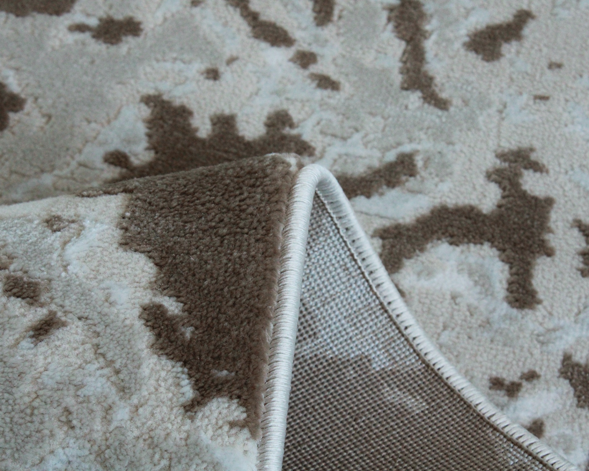 Tapete com padrão castanho e creme, detalhe da costura e base antiderrapante