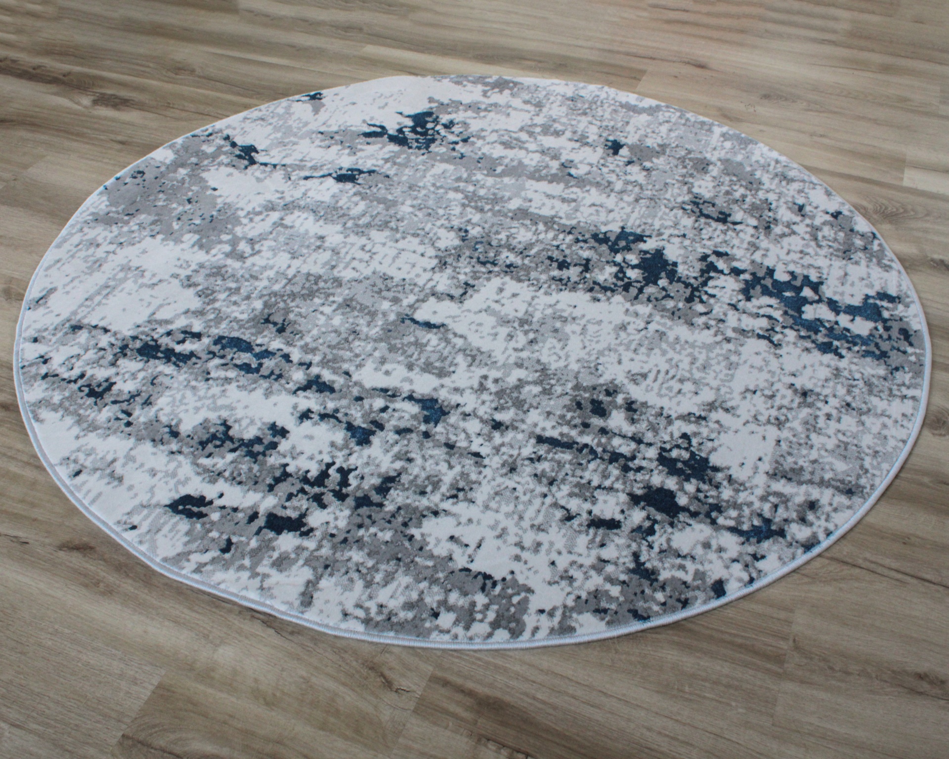 Tapete redondo com padrão cinza, branco e azul escuro em piso de madeira