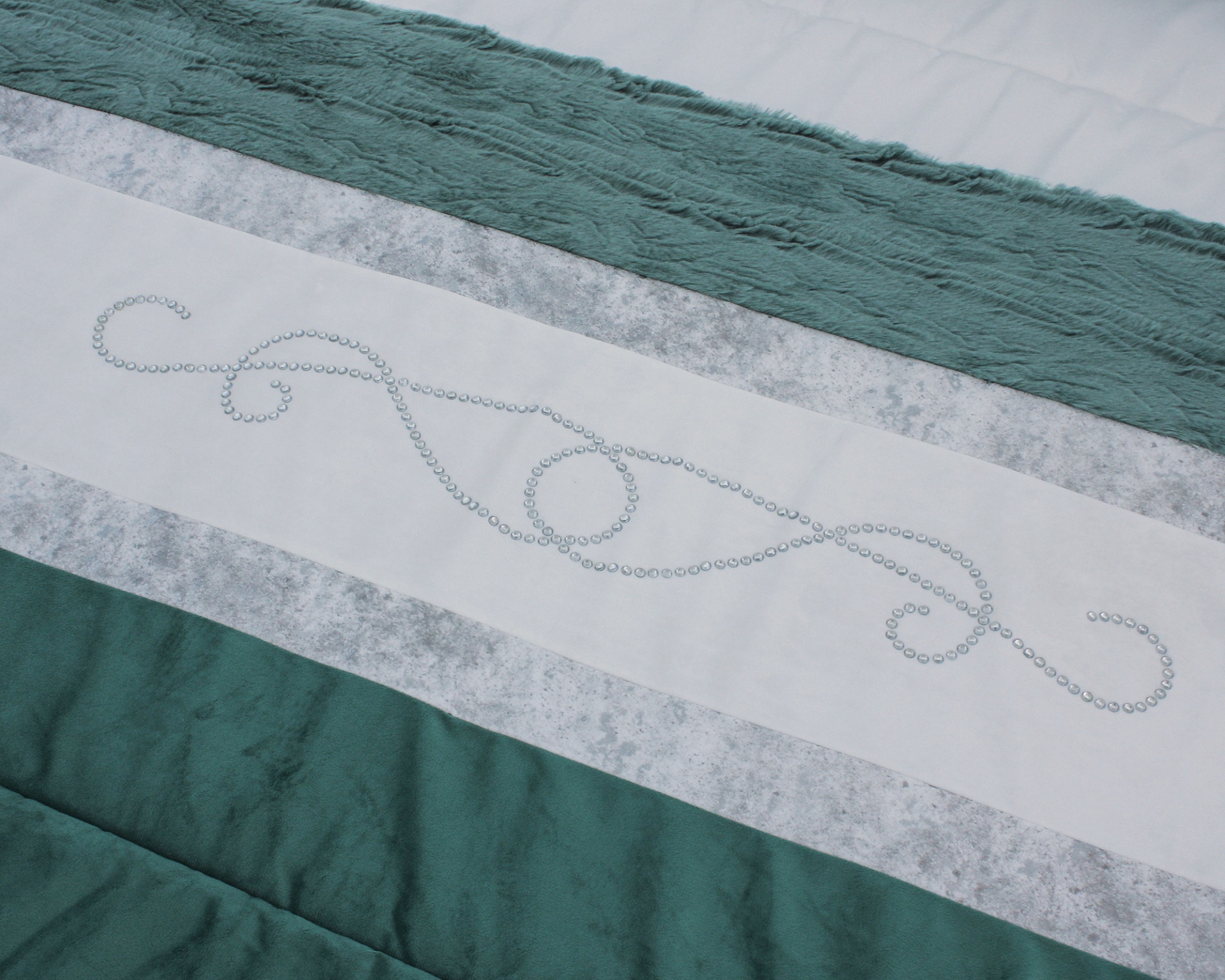 Têxtil para cama com faixas verdes, brancas e cinzentas e padrão de contas em espiral.