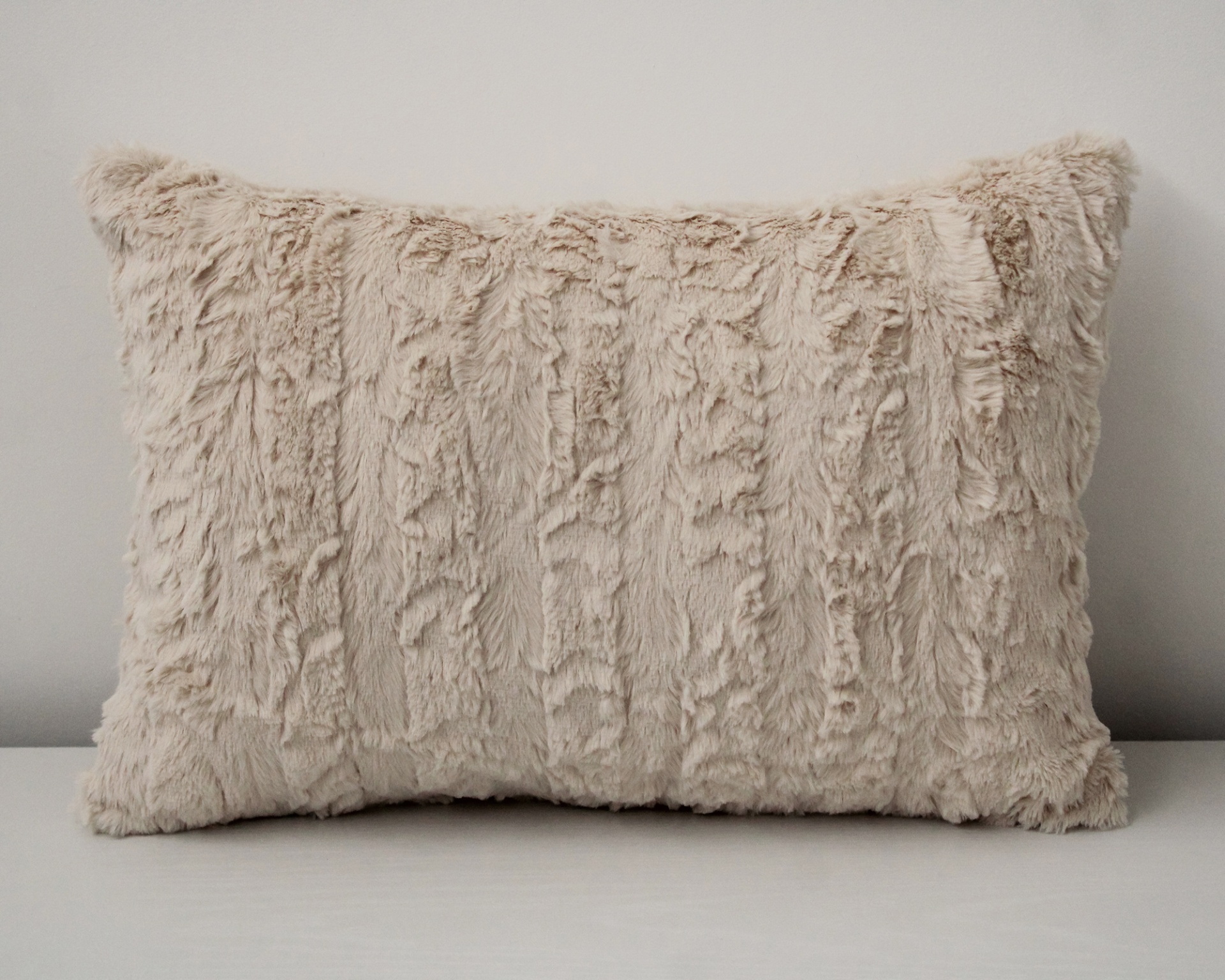 Almofada retangular de pelúcia creme com textura macia e padrão irregular