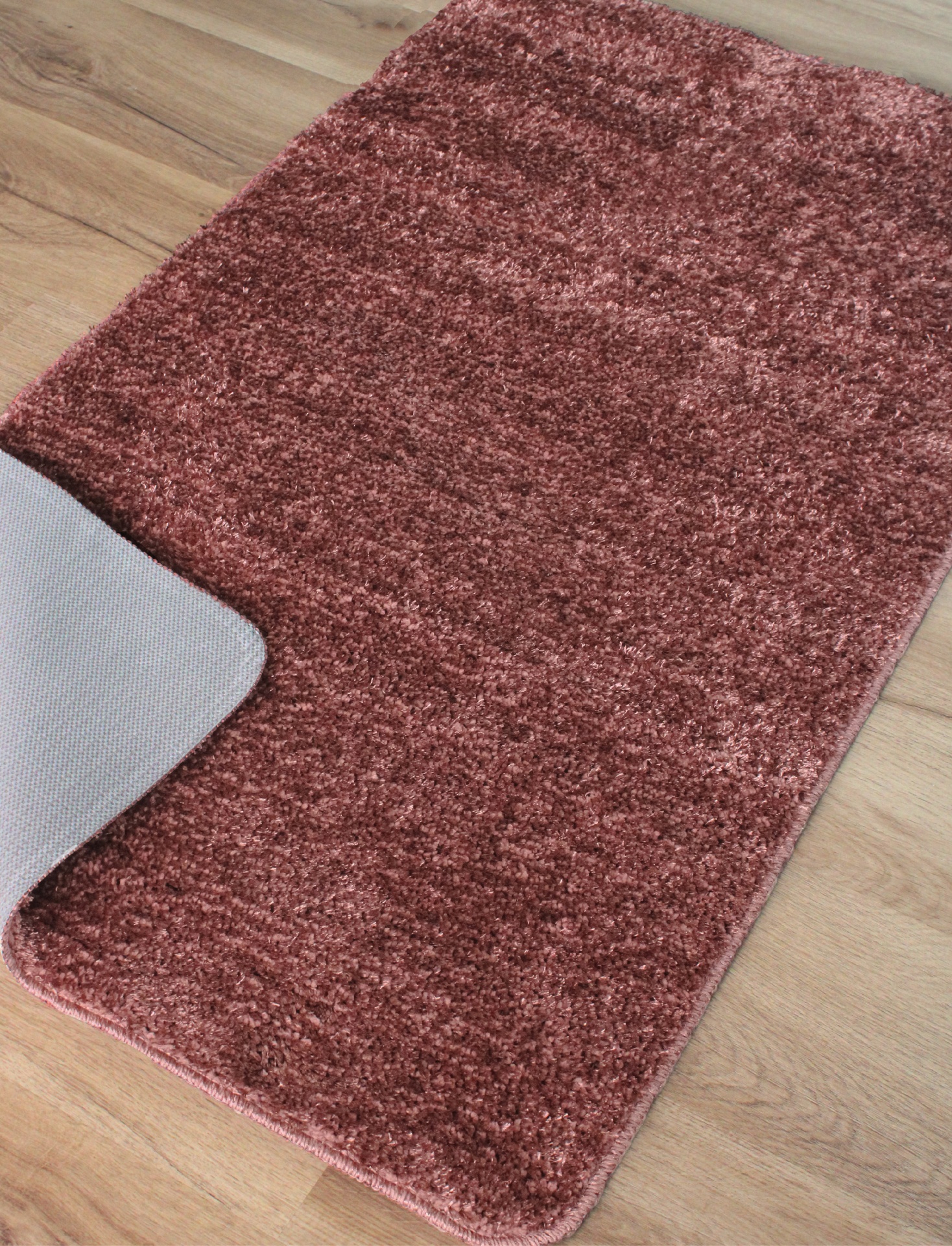 Tapete vinho retangular com pelo curto e base antiderrapante cinza sobre chão de madeira.