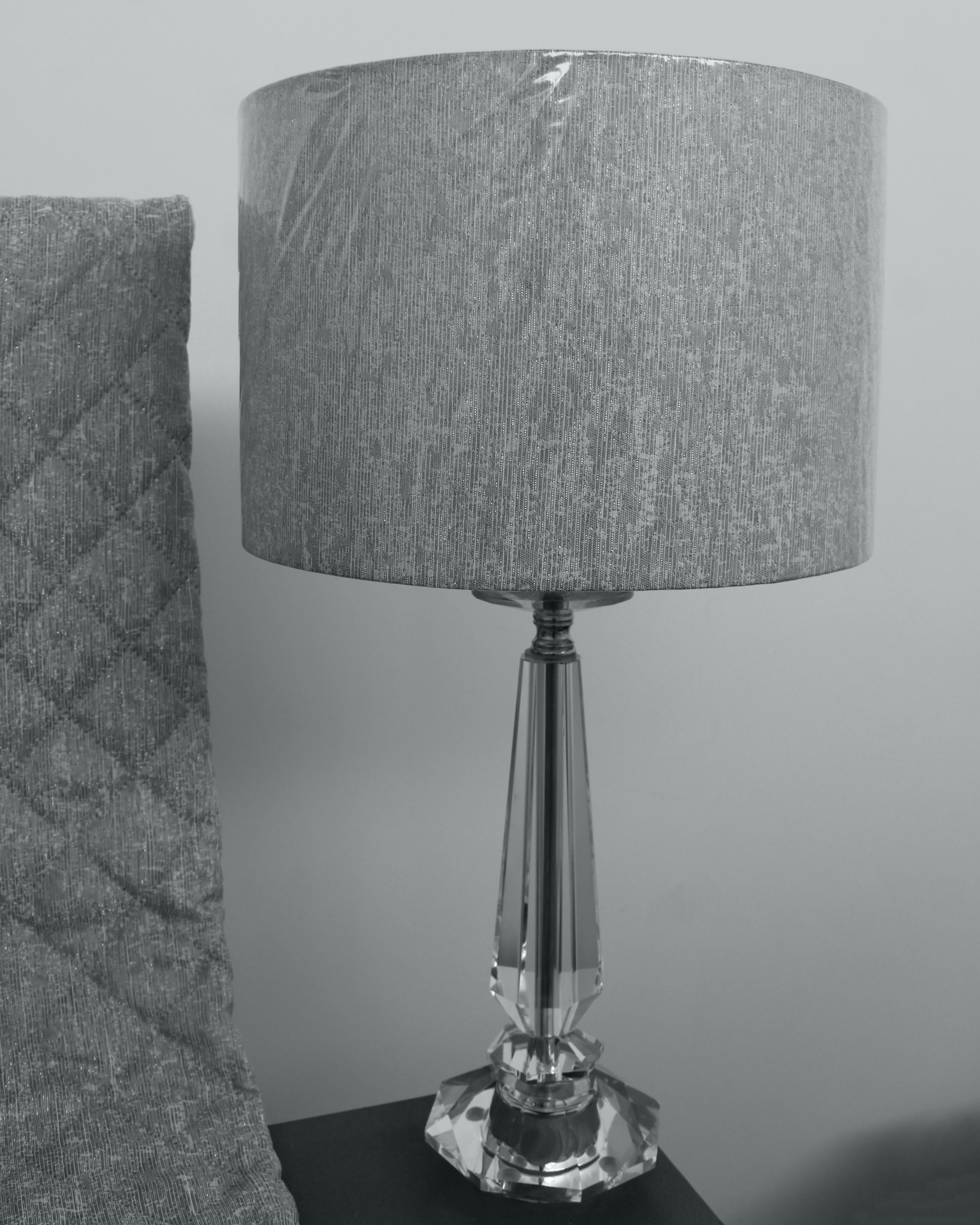 Candeeiro de mesa com base de vidro e abajur cinzento junto a tecido cinzento com padrão