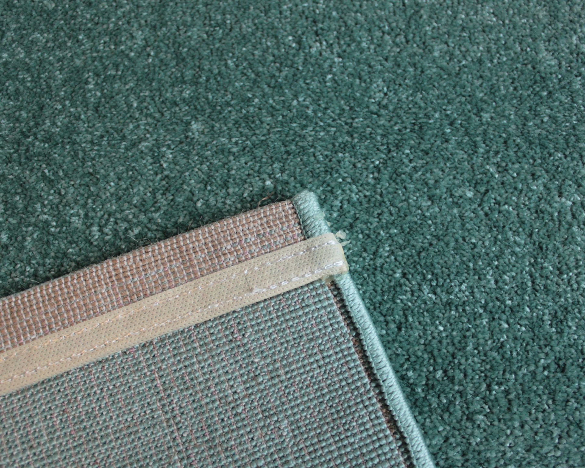 Tapete verde felpudo com canto virado mostrando verso tecido e bordado