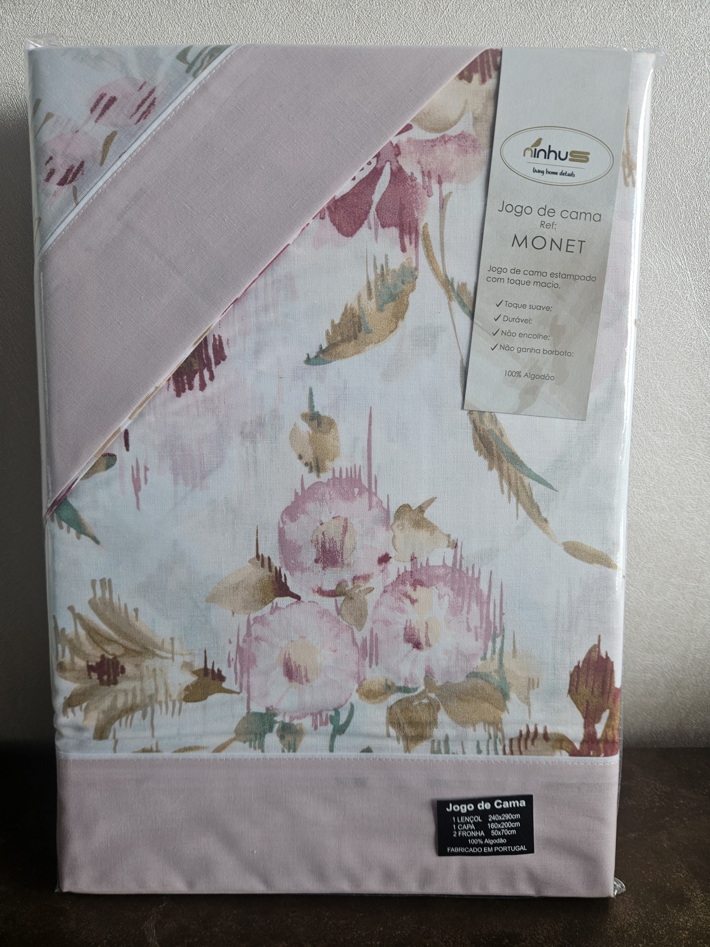 Embalagem de jogo de cama estampado com flores em tons rosa, bege e verde e etiqueta com informações.