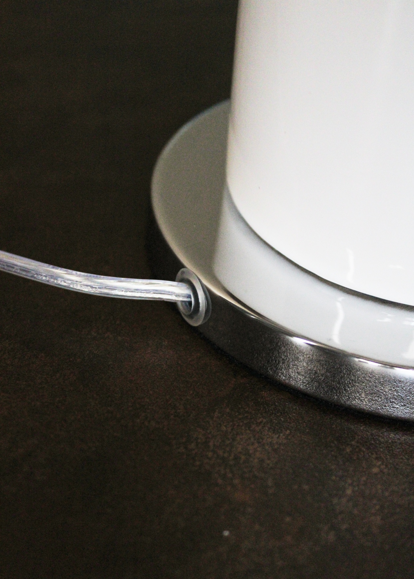 Base de aparelho branco com acabamento inox e cabo transparente sobre superfície escura