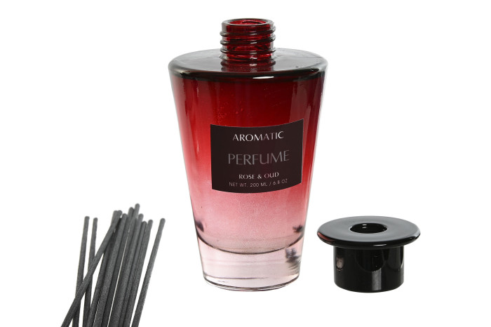 Frasco de perfume vermelho e rosa com tampa preta e varetes aromáticas pretas