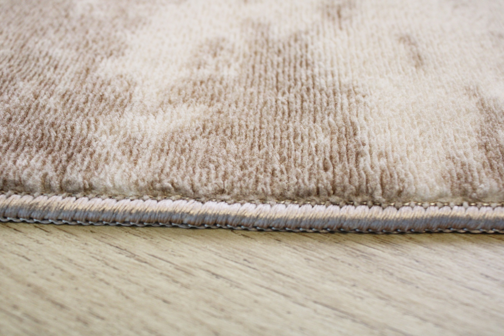 Tapete bege com padrões claros e costura cinza sobre chão de madeira clara