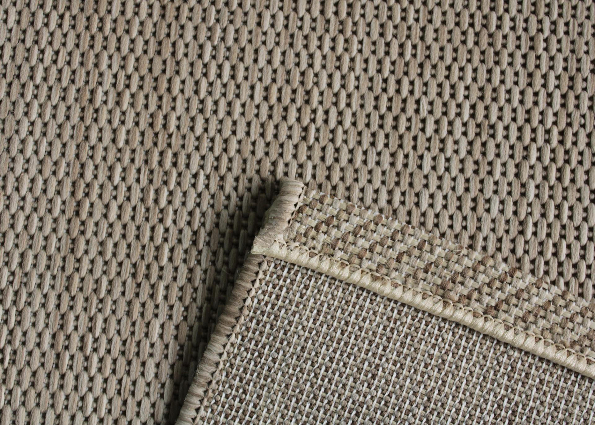 tapete bege com padrão trançado e canto virado mostrando verso cinza