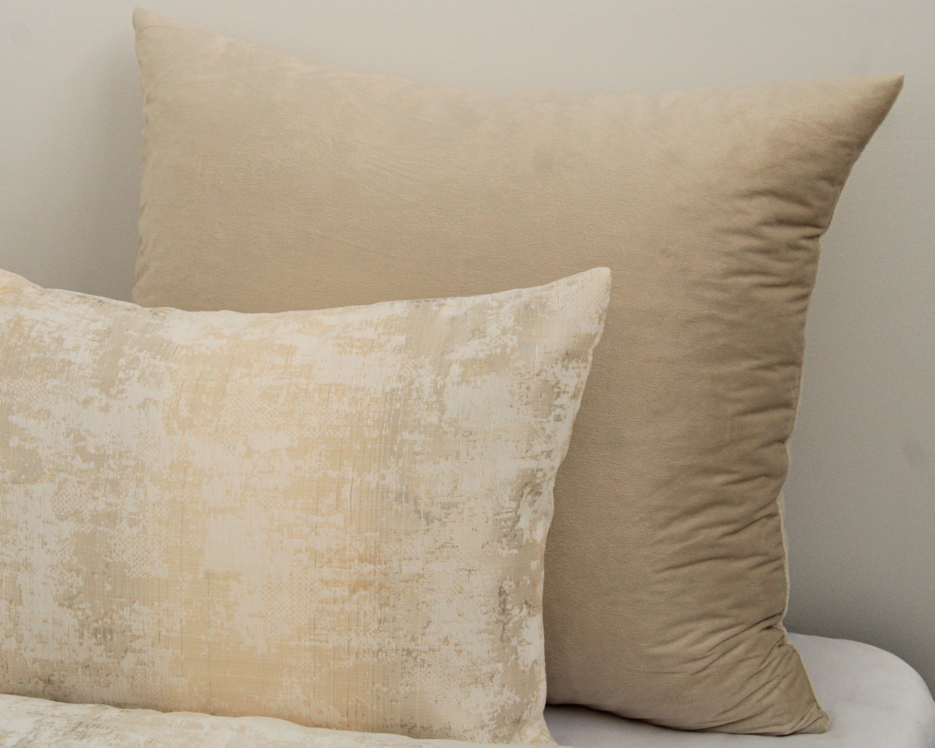 Duas almofadas bege, uma lisa e outra com padrão abstrato
