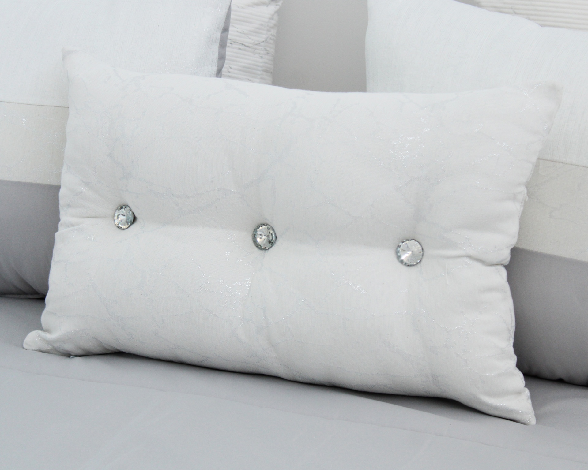 Almofada branca com botões brilhantes sobre cama cinza e branca