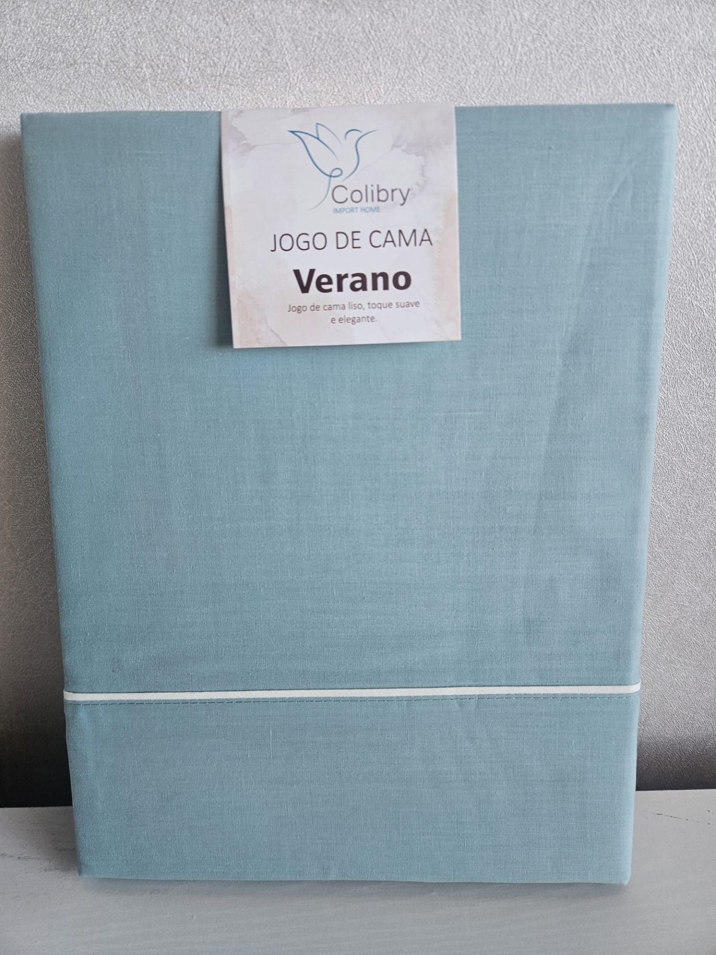Conjunto de roupa de cama azul claro da marca Colibry com etiqueta Jogo de Cama Verano