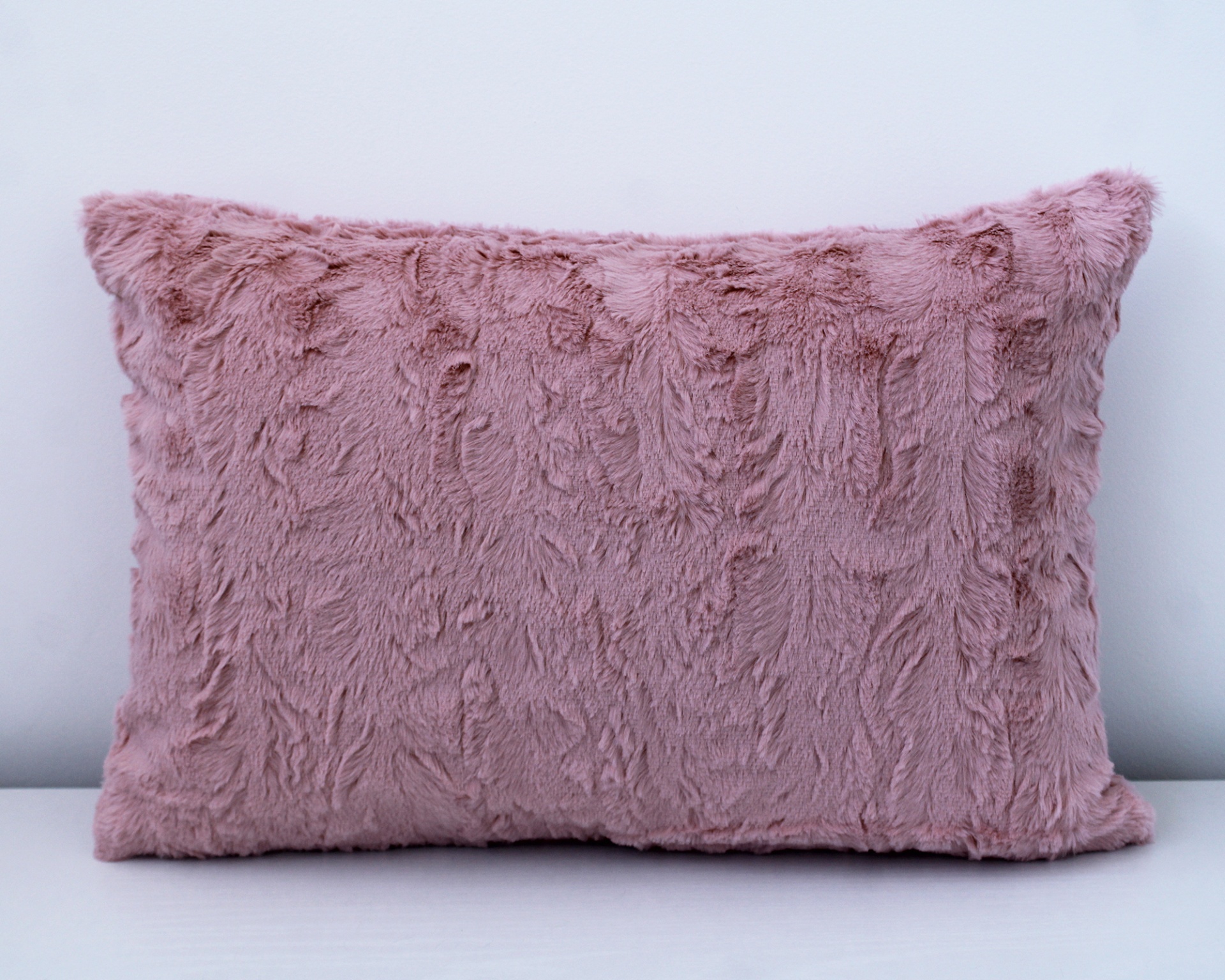 Almofada rosa felpuda retangular sobre superfície branca