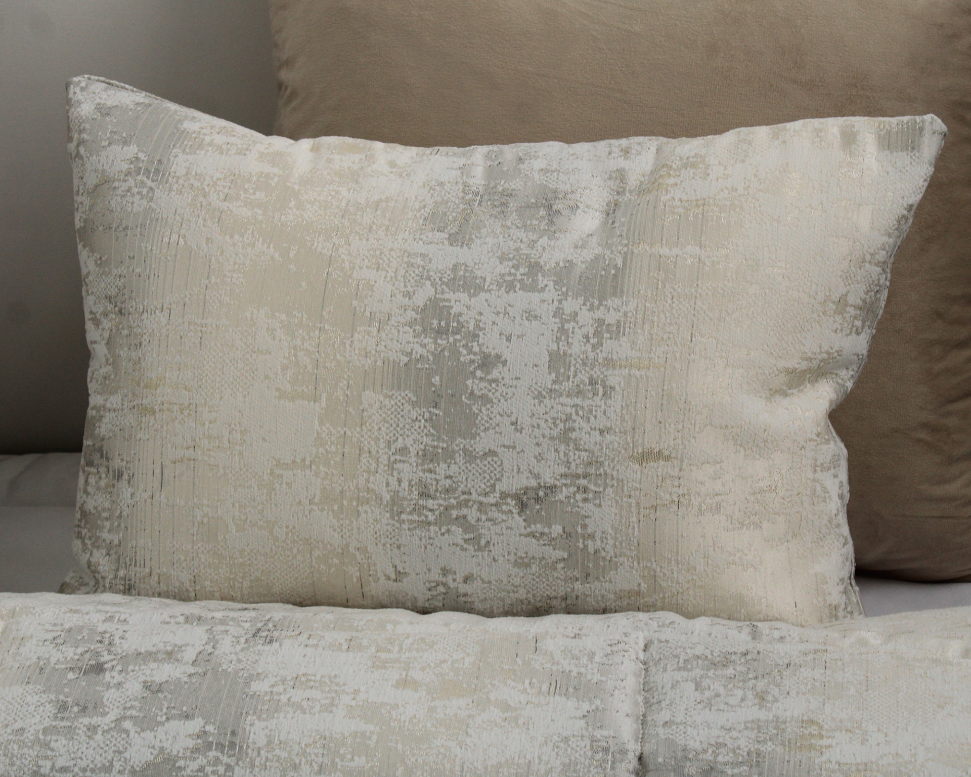 Almofada e edredão com padrão abstrato em branco, bege e cinza sobre sofá castanho claro