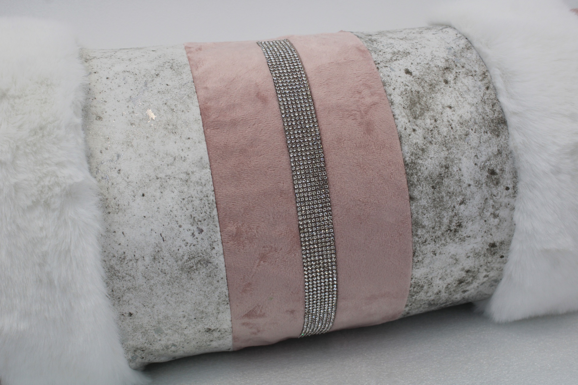 Almofada decorativa com textura branca felpuda e faixa rosa com pedraria prateada