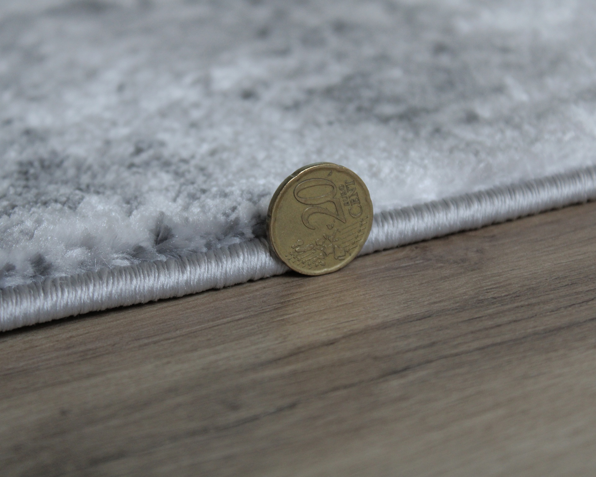 Tapete cinzento com padrão abstracto ao lado de moeda de 20 cêntimos sobre chão de madeira