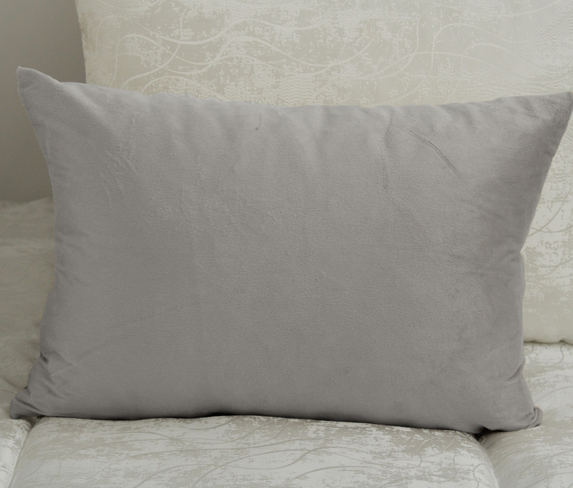 Travesseiro cinzento sobre cadeira ou sofá com padrão florido claro