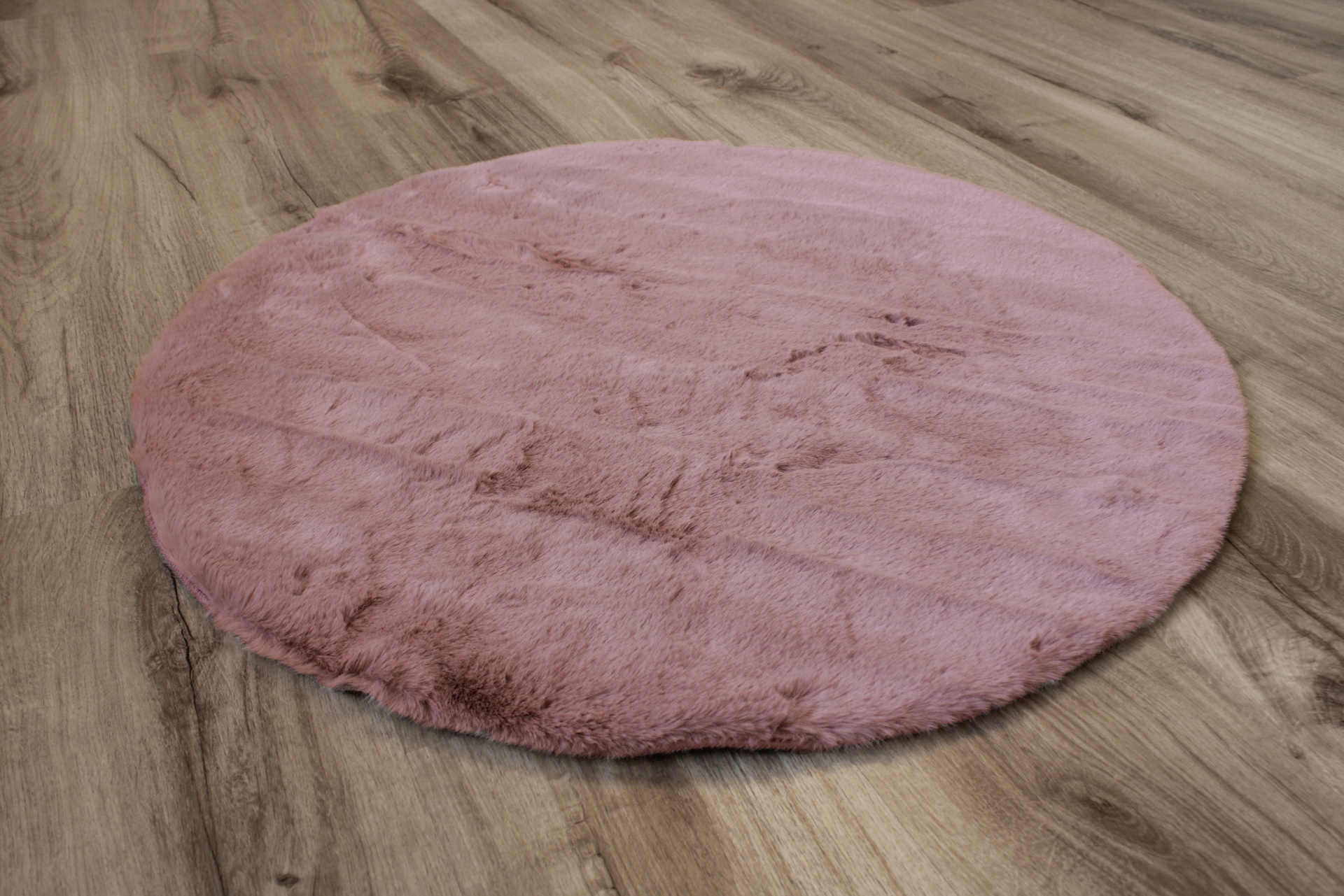 Tapete redondo rosa peludo sobre chão de madeira